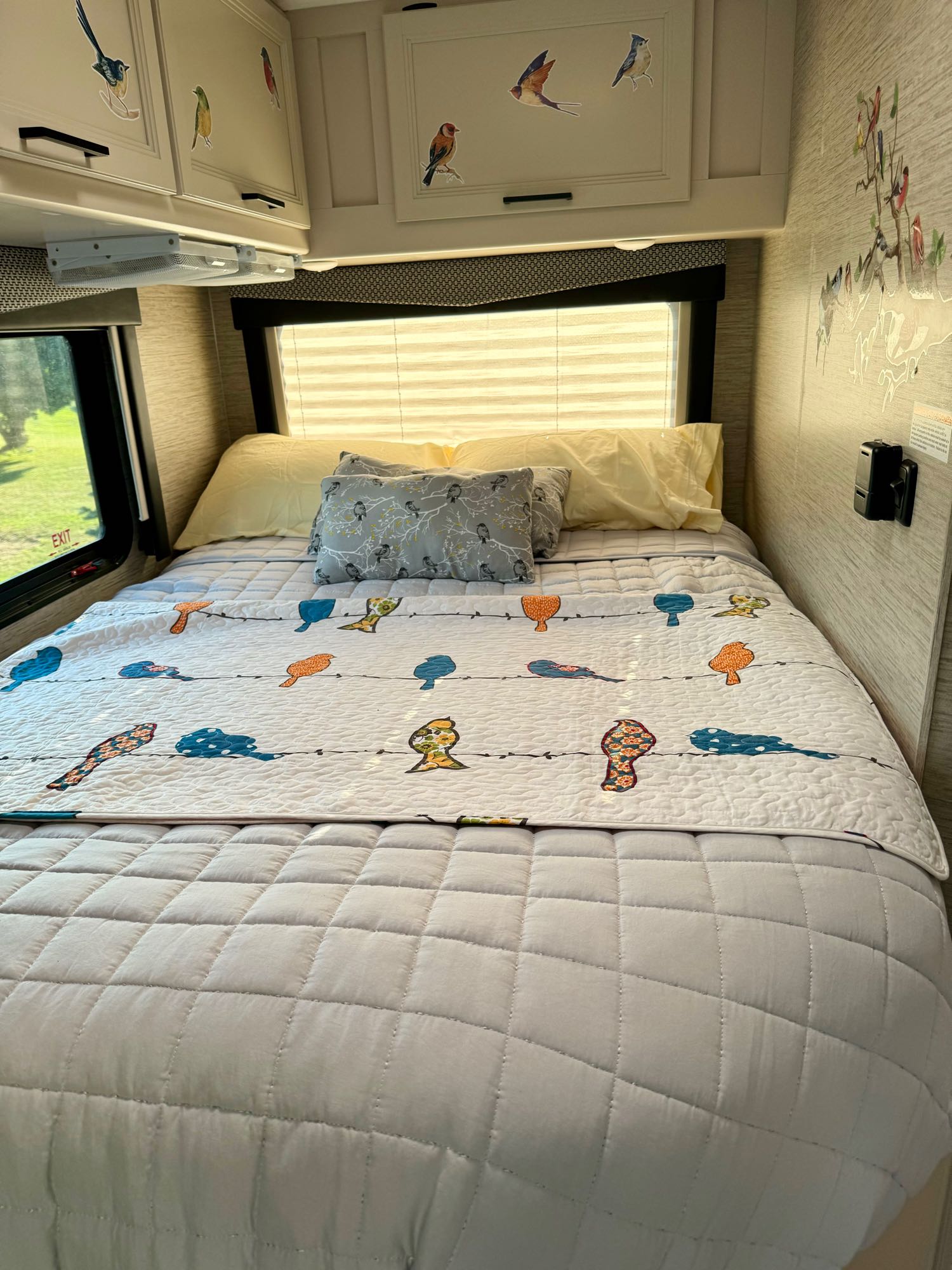 This RV rental bedroom features a cozy bed with a quilted bird-themed blanket, colorful bird decals on walls & cabinets.. Thor Freedom Elite 2022