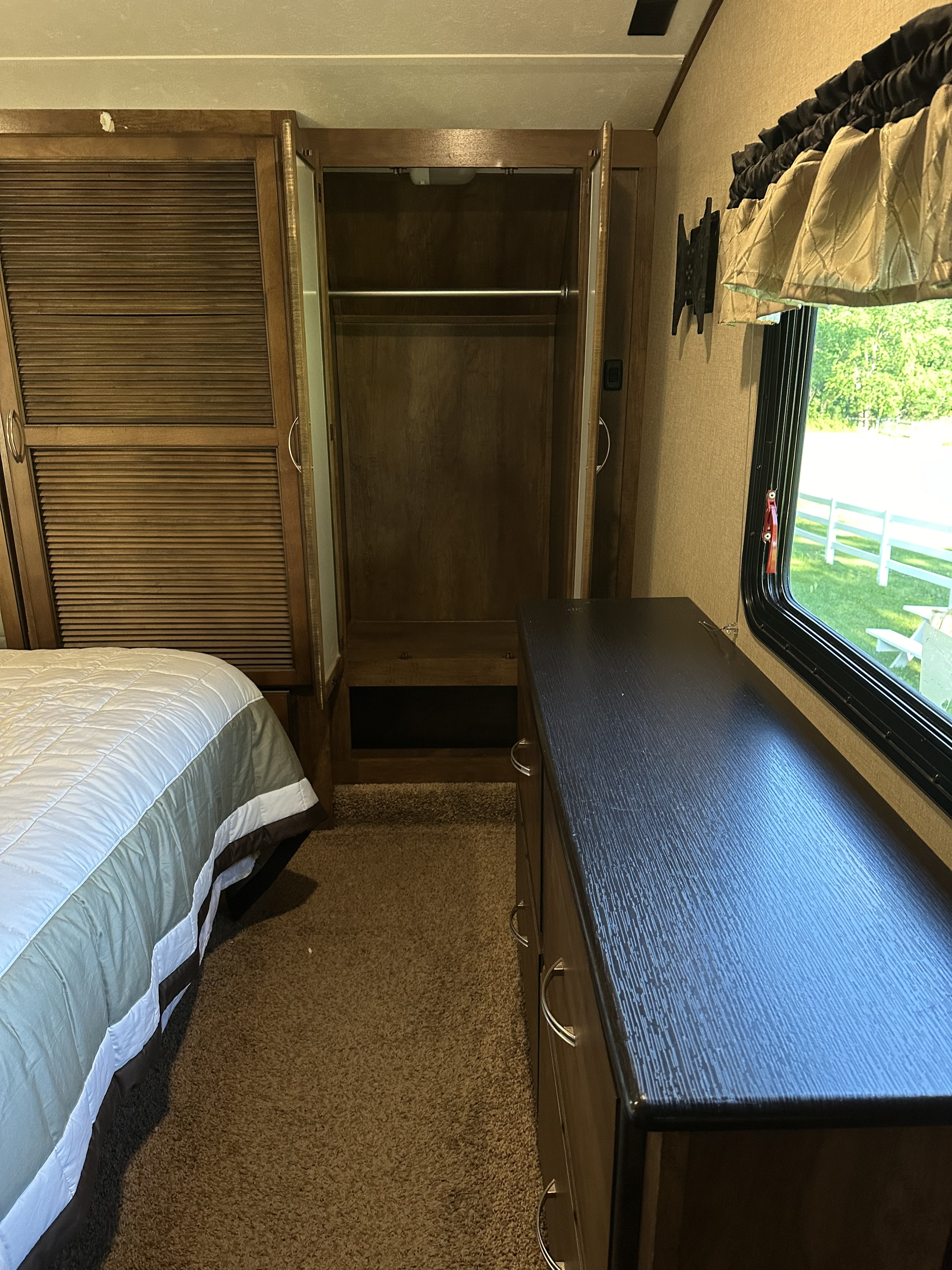 Inside an RV rental bedroom: features a comfortable bed, open closet, and dresser. Window offers outdoor view.. Forest River Coachmen Chapparal 2016