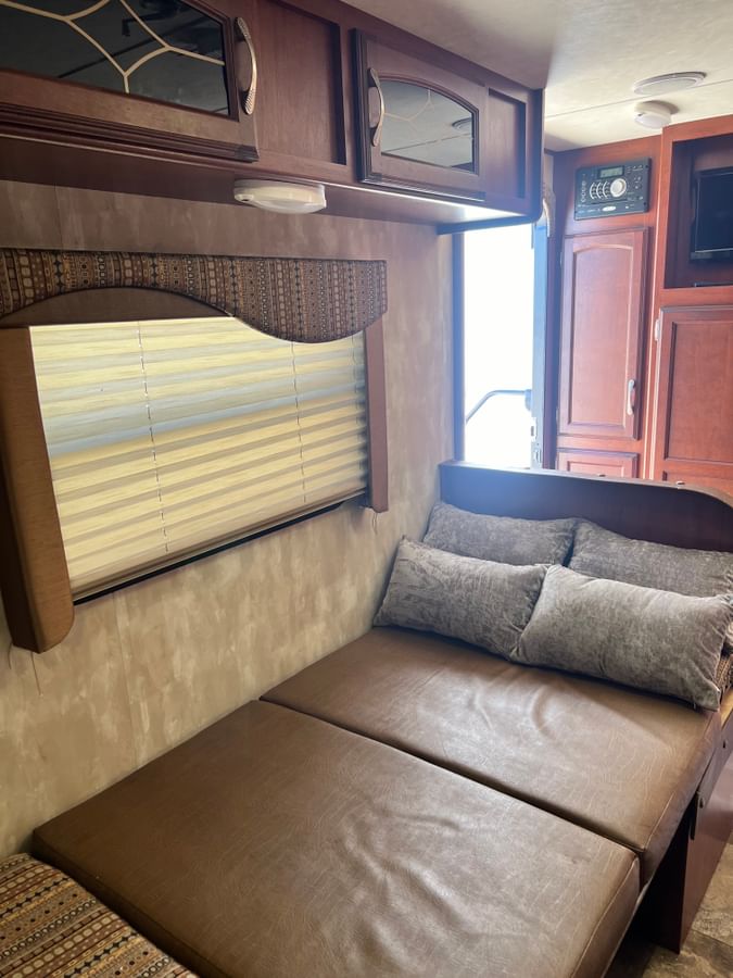 Inside an RV rental: a cozy seating area converts to a bed, with overhead cabinets, a window, and wood accents.. Winnebago 1801FB 2015