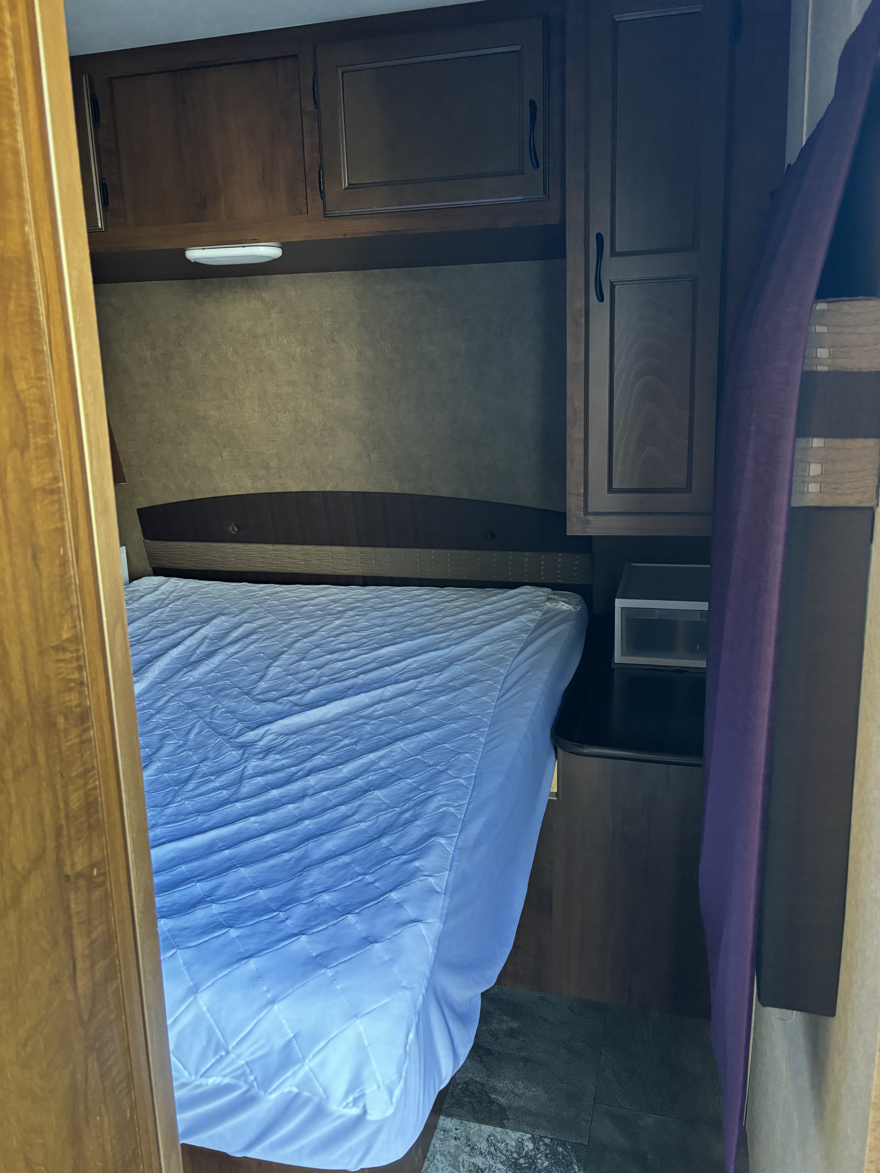RV rental bedroom showcasing a light blue bed, wooden overhead cabinets, and a convenient nightstand. Ready for travel!. Jayco Jay Flight 2015