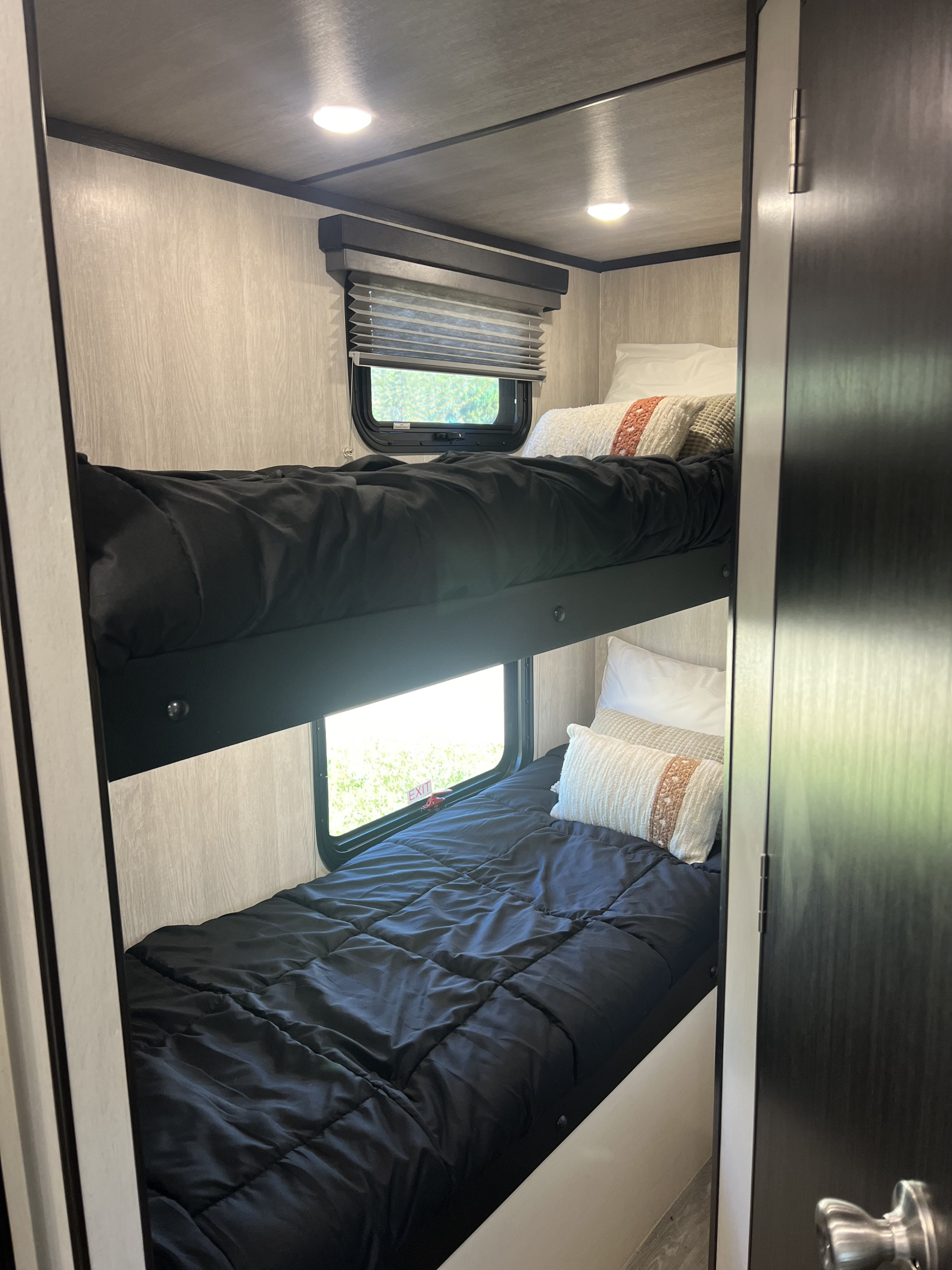 RV rental interior: Two bunk beds with black bedding, pillows, and windows create a compact sleeping area, lit by overhead lights.. Genesis Northland 2024