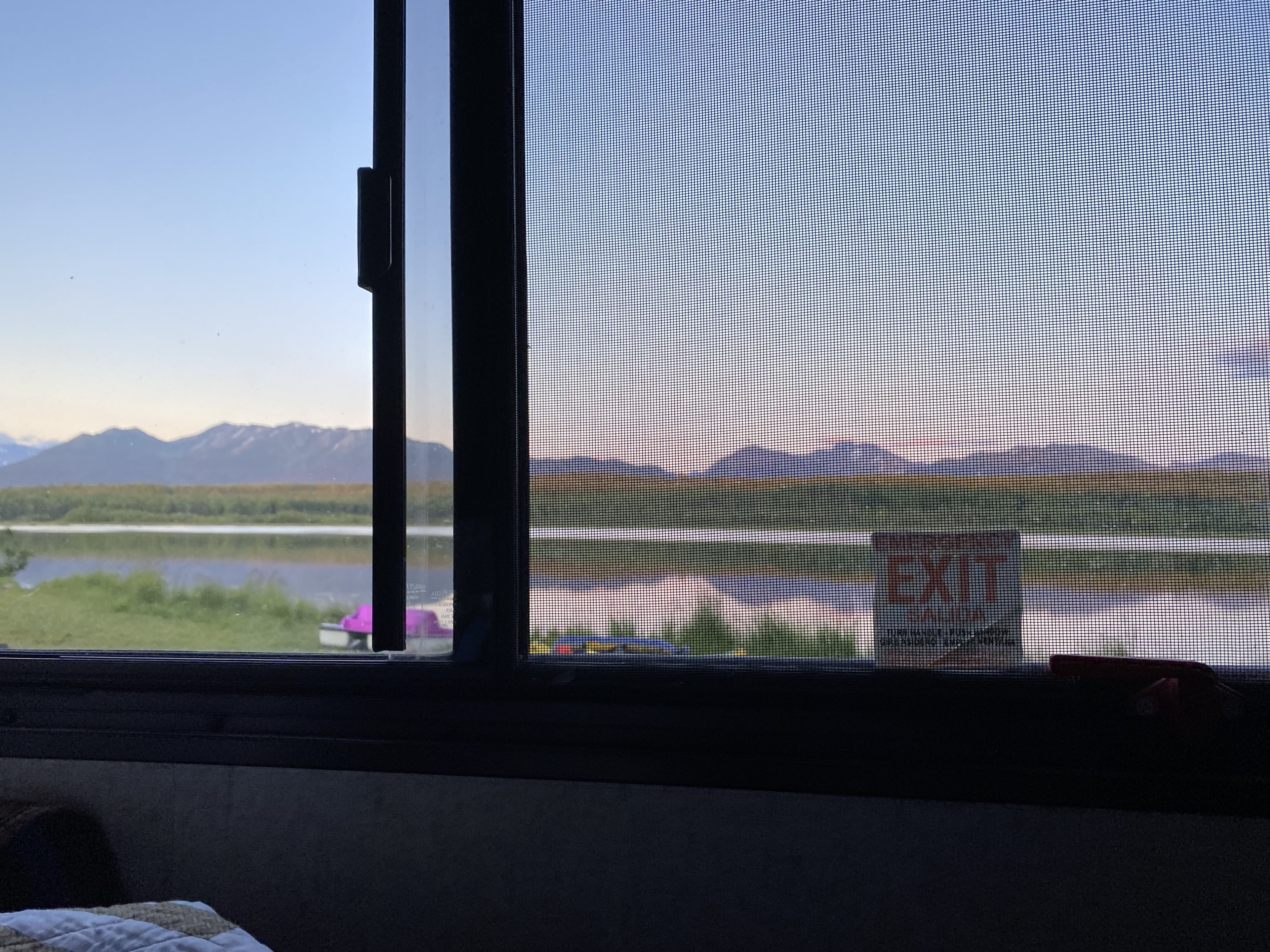 Relaxing RV rental view of a serene lake and distant mountains. The window screen and an "EXIT" sign offer unique indoor context.. Forest River Sunseeker 2018