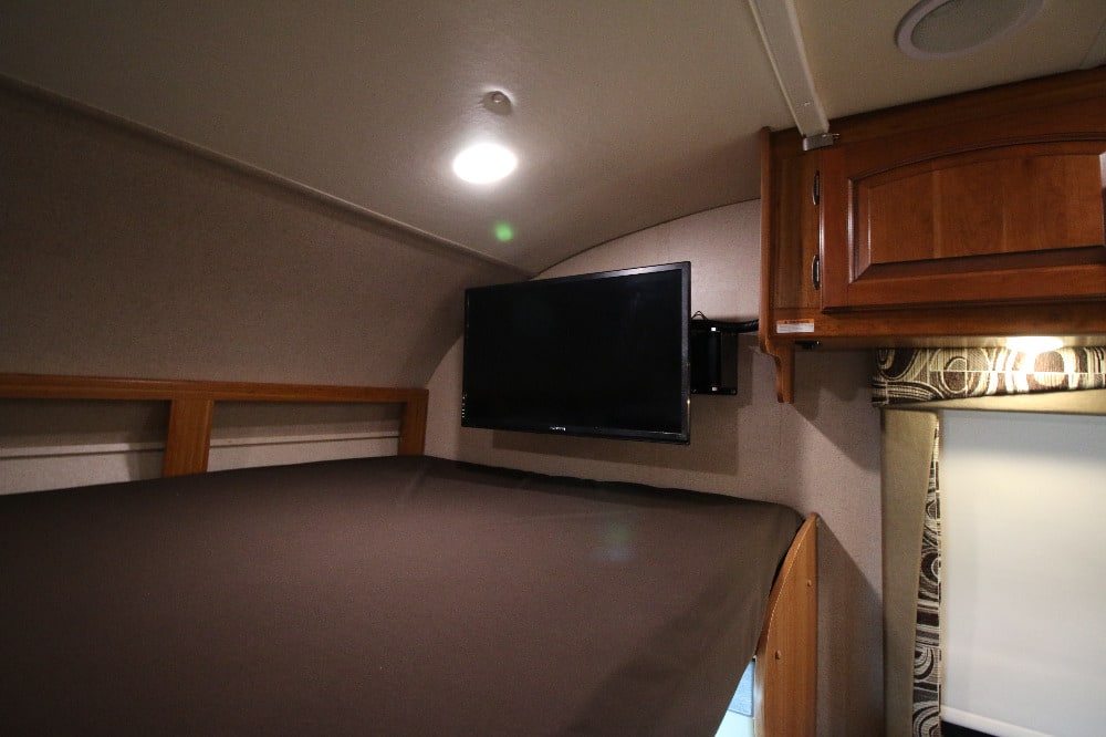 Inside an RV rental: a bunk bed with dark mattress, mounted TV, and wood cabinetry. Ideal for families.. Jayco Greyhawk 2017