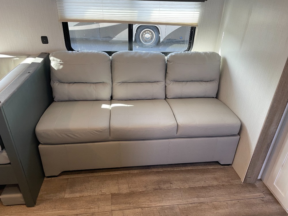 Inside an RV rental: a comfortable light gray sofa with three cushions under a window, on wood-look flooring.. Keystone RV Eddie Bauer 34bsbh 2024