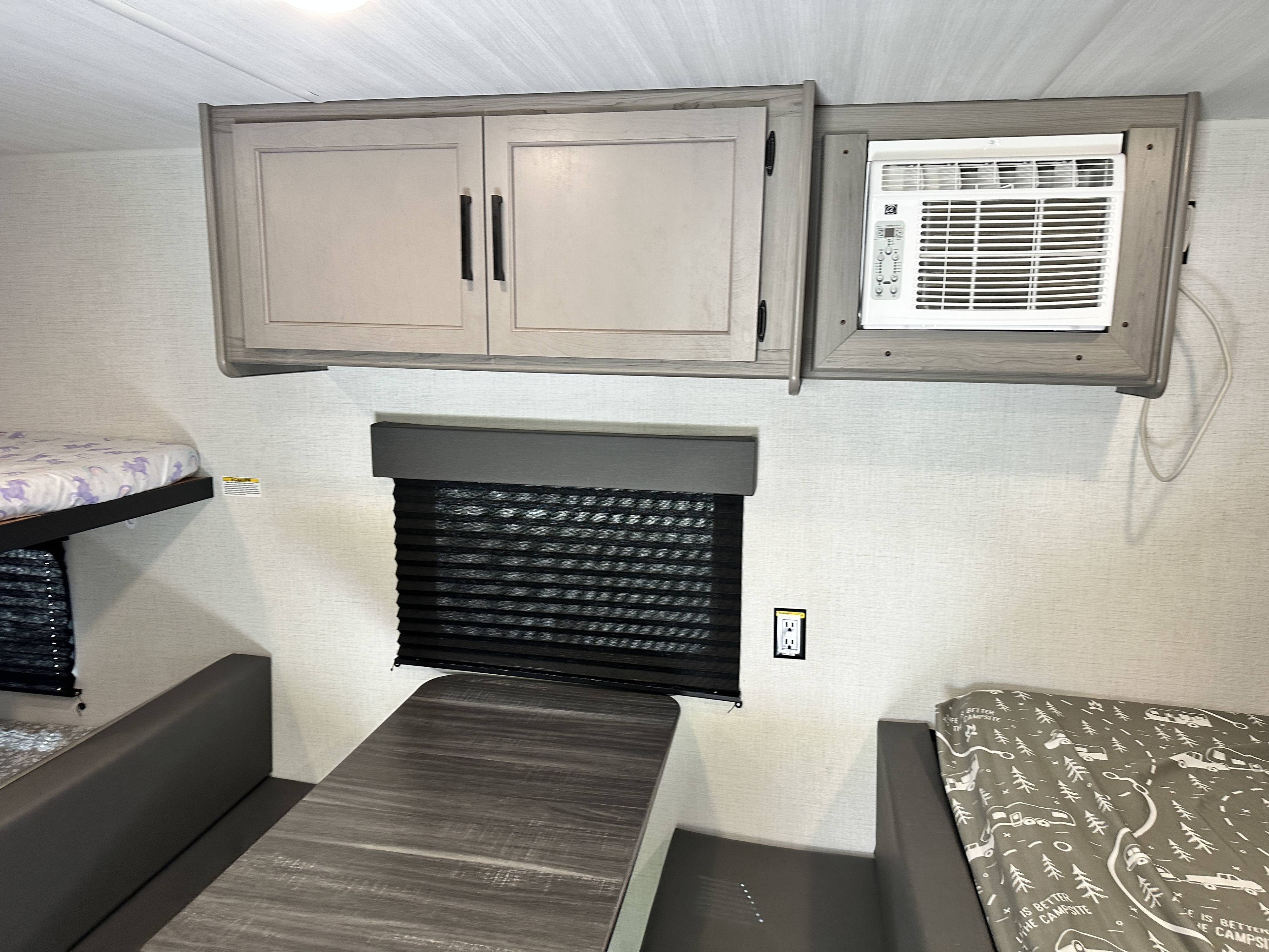 Spacious RV rental interior featuring bunk beds, a dinette, overhead cabinets, window blind, and AC unit for comfortable travel.. Keystone RV Hideout Sport 2024
