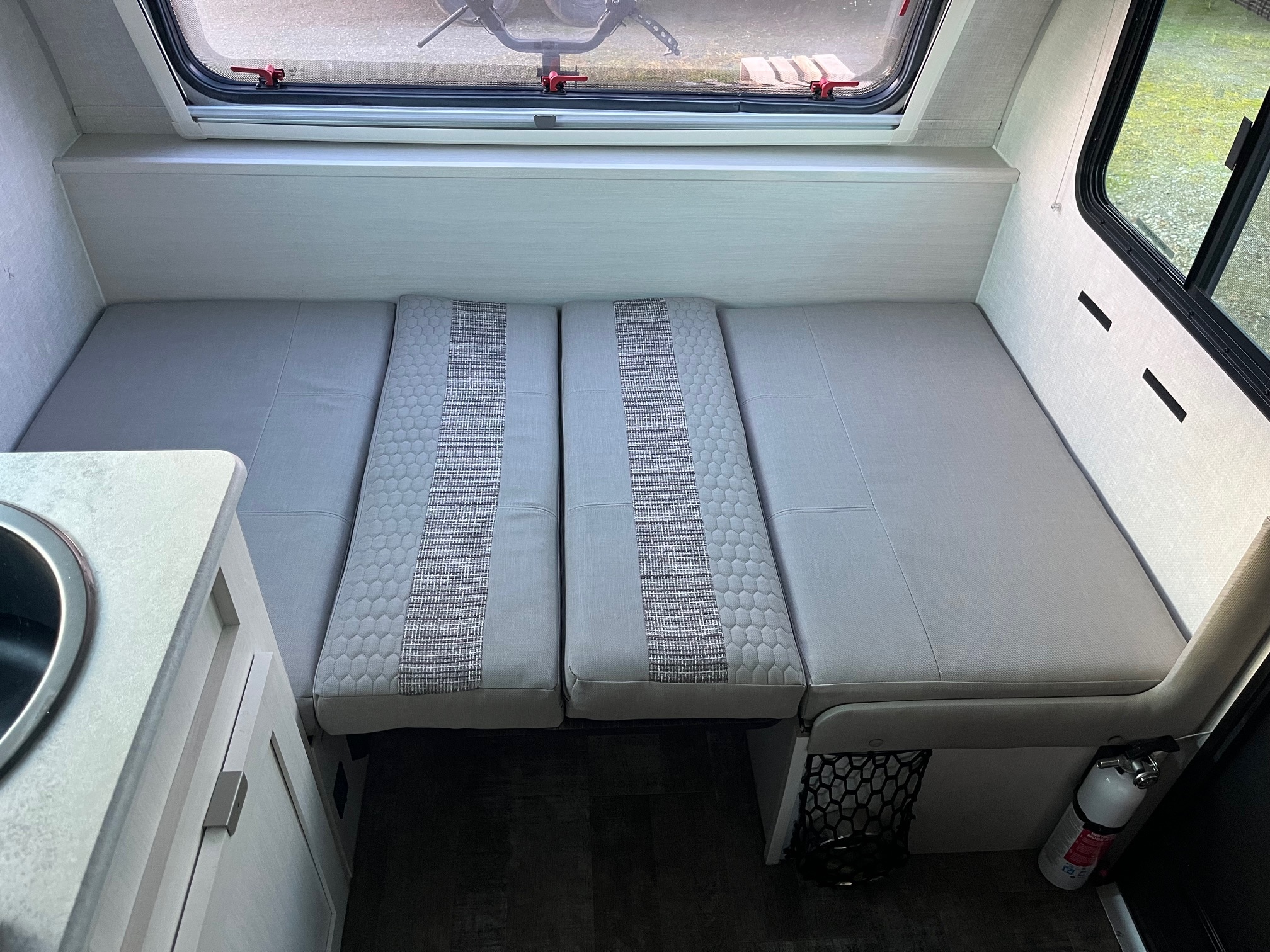 Bright RV rental interior shows a dinette with light gray cushions (convertible to bed), visible sink, and fire extinguisher.. Forest River R-Pod 171 2022