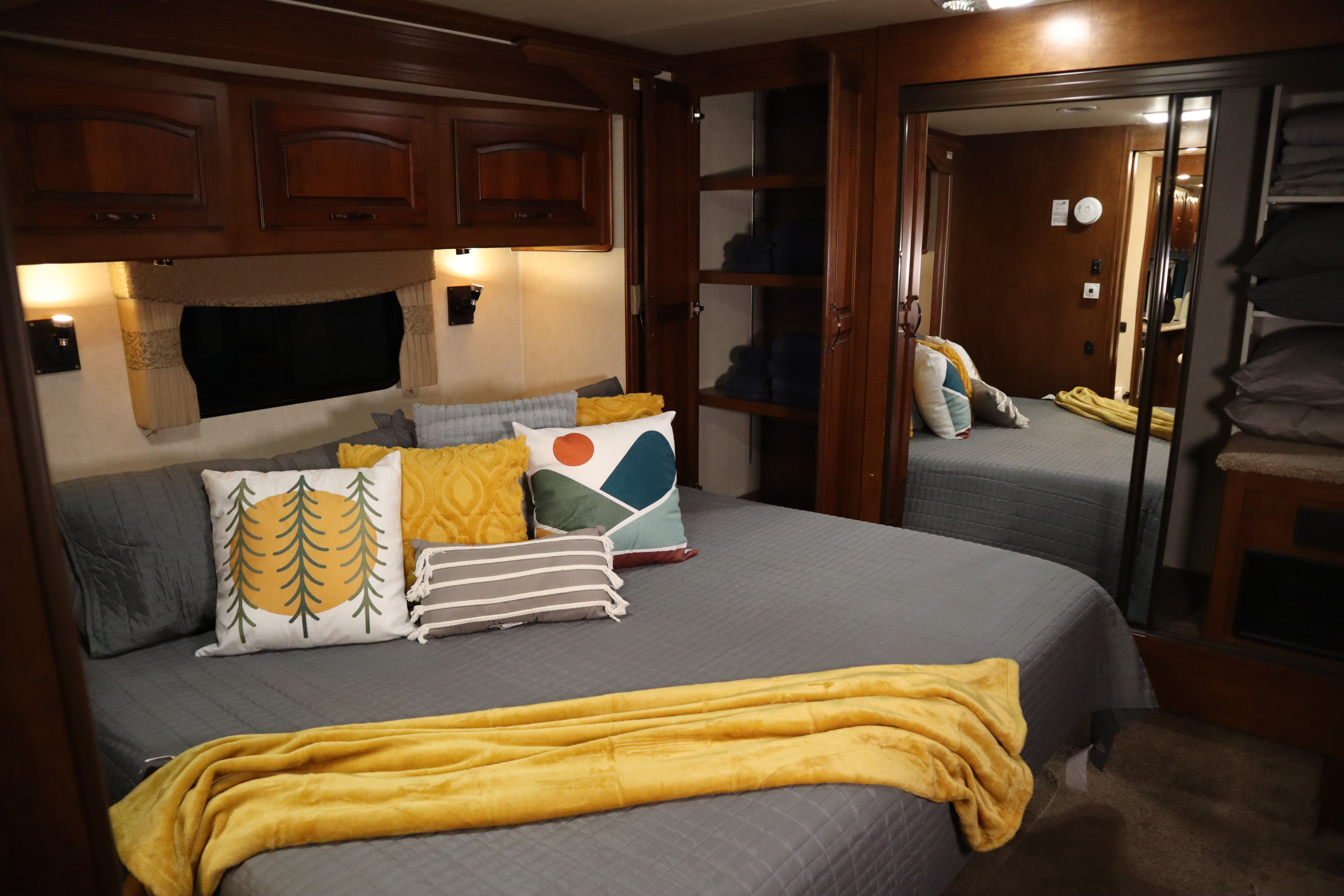 Cozy RV rental bedroom with warm lighting, plush bed, decorative pillows, and built-in storage. Perfect for a comfortable stay.. Coachmen Cross Country Sportscoach 2012