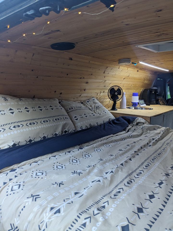 This cozy RV rental bed and wood-paneled interior features a small sink area, perfect for van life.. Ford Econoline 150 1999