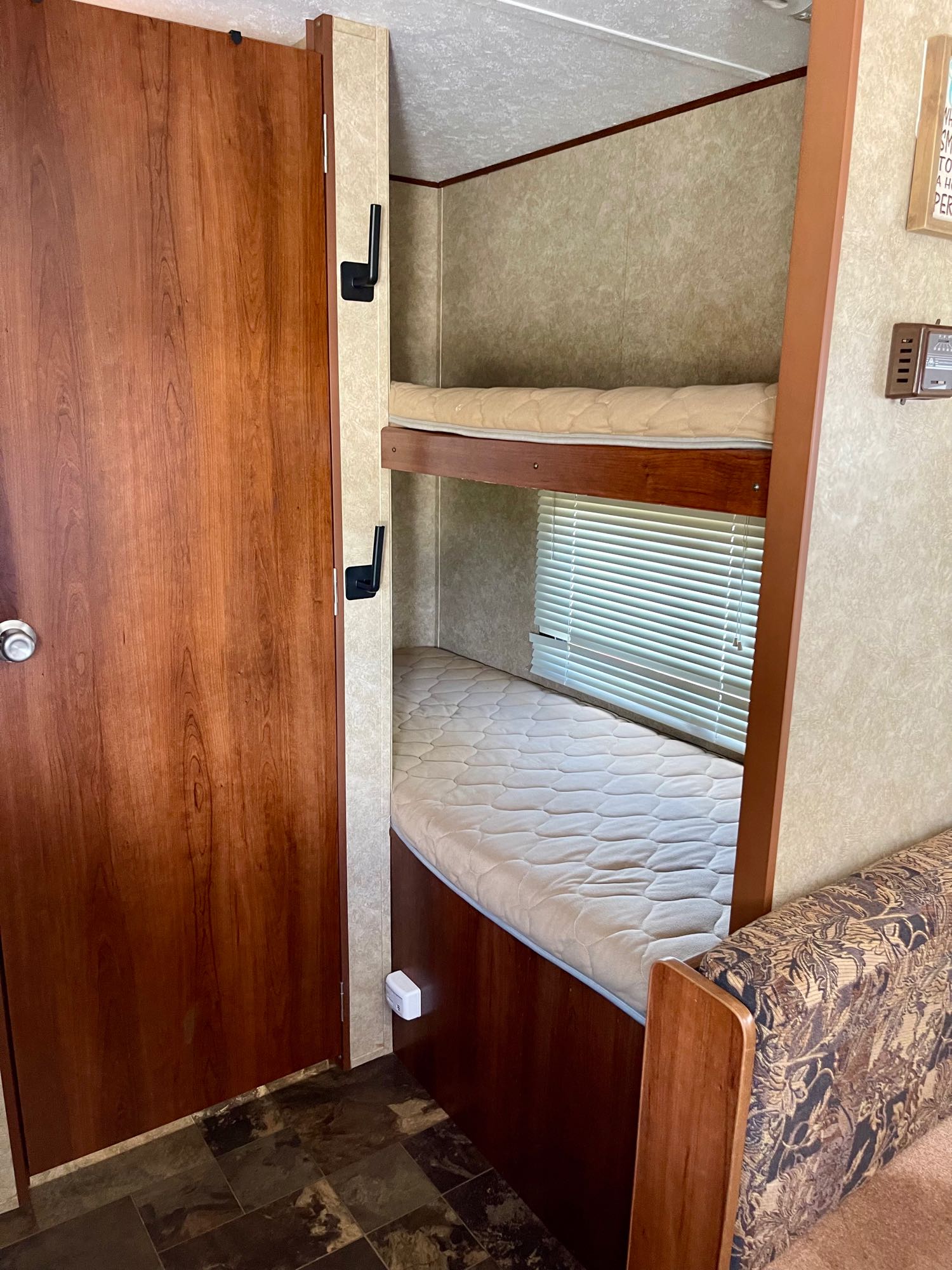 Cozy RV rental interior: wooden door, bunk beds with mattresses, window, and patterned seating area.. Avenger ATI 2014