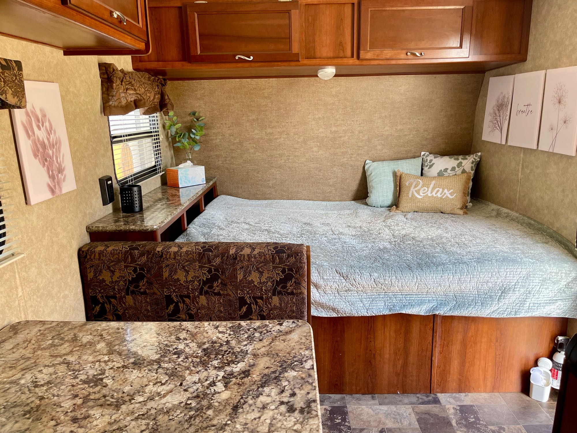 This cozy RV rental interior features a bed, dinette, cabinets, and decorative art, designed for a relaxing travel experience.. Avenger ATI 2014