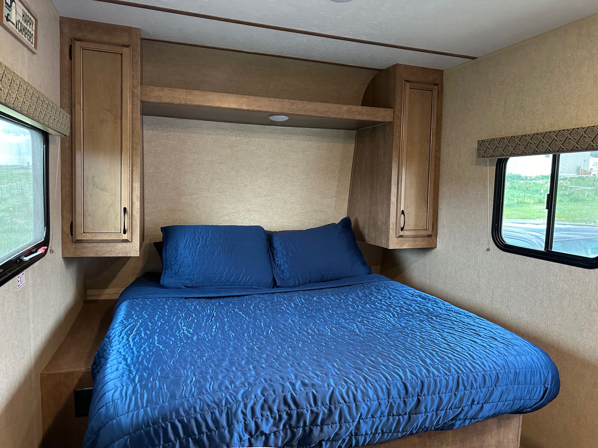 Cozy RV rental bedroom featuring a blue bed, overhead cabinets, and side windows.. Starcraft Launch Outfitter Extreme 2018