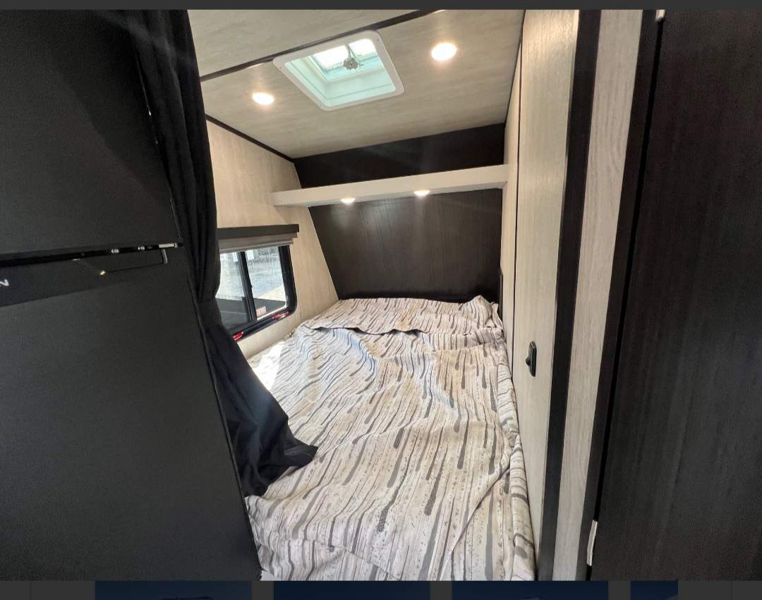 RV rental interior featuring a compact bedroom with patterned bed, window, refrigerator, and cabinet storage.. Genesis Supreme Rv Blazen 2015SSXL 2025