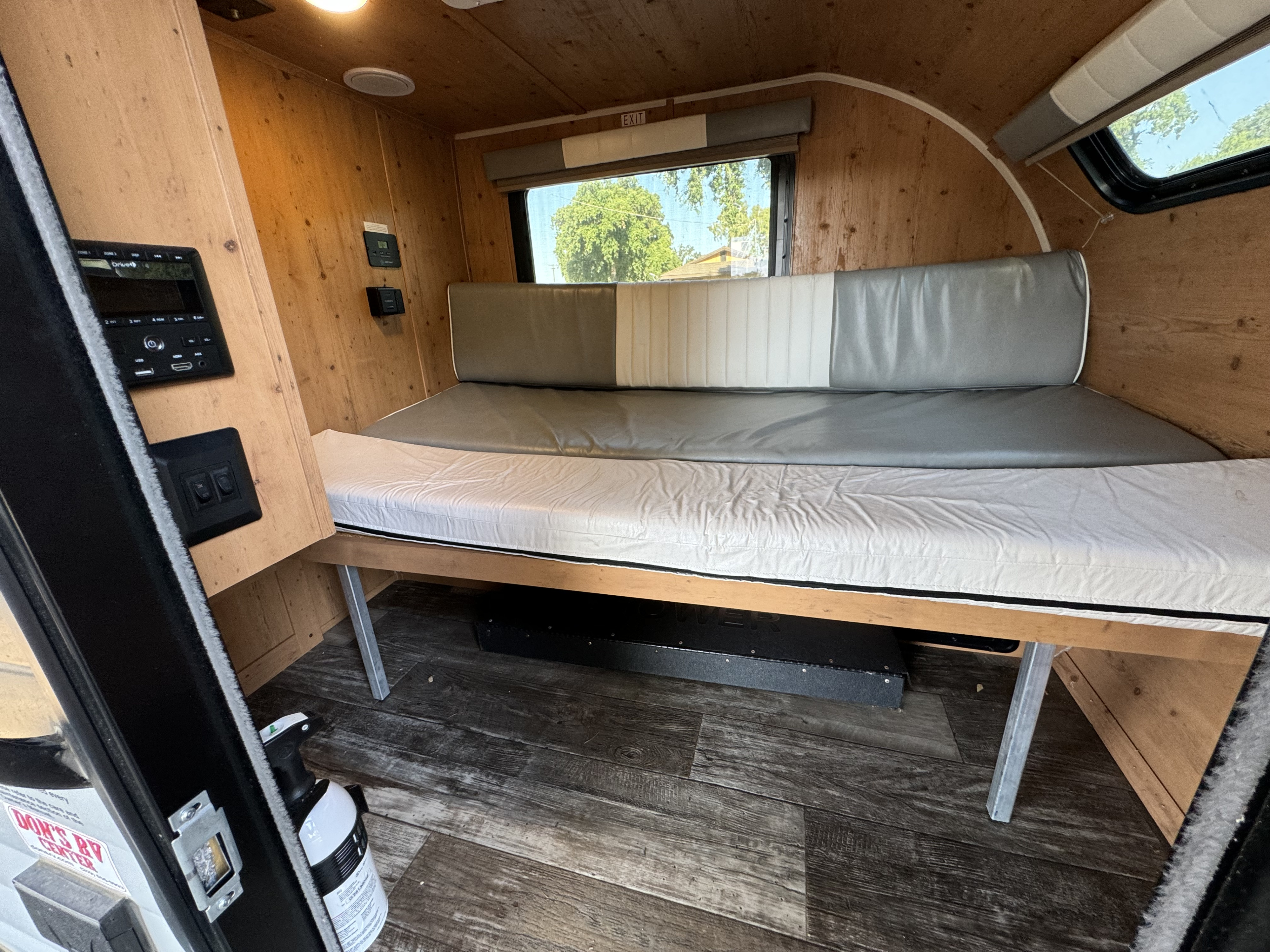 Interior of an RV rental featuring a wood-paneled bed/bench, window, and control panel for a cozy mobile living space.. Sunset Park RV SunRay 2022