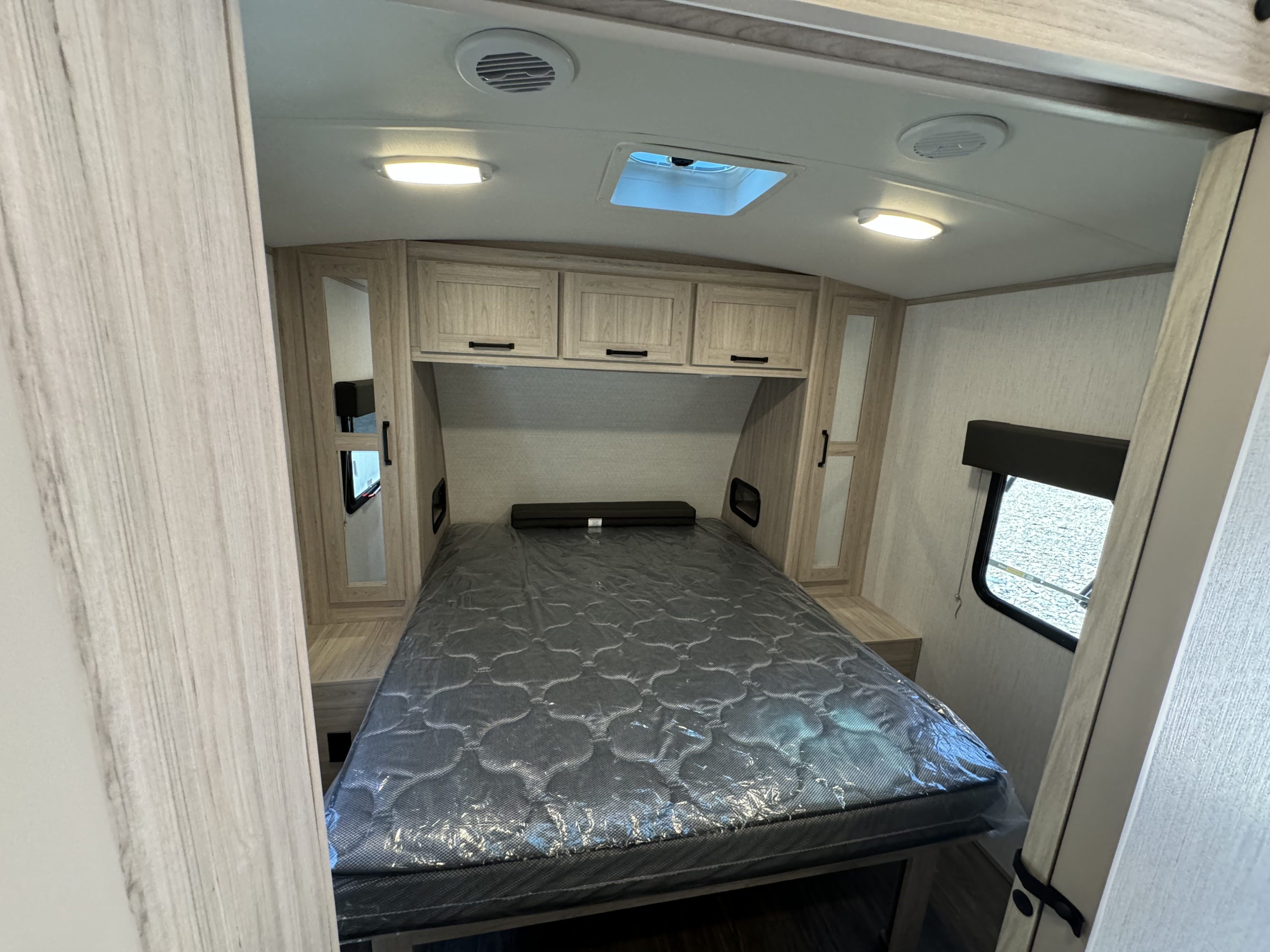 RV rental bedroom with new plastic-wrapped mattress, overhead cabinets, window, skylight, and vents.. Cruiser RV Shadow Cruiser 2023