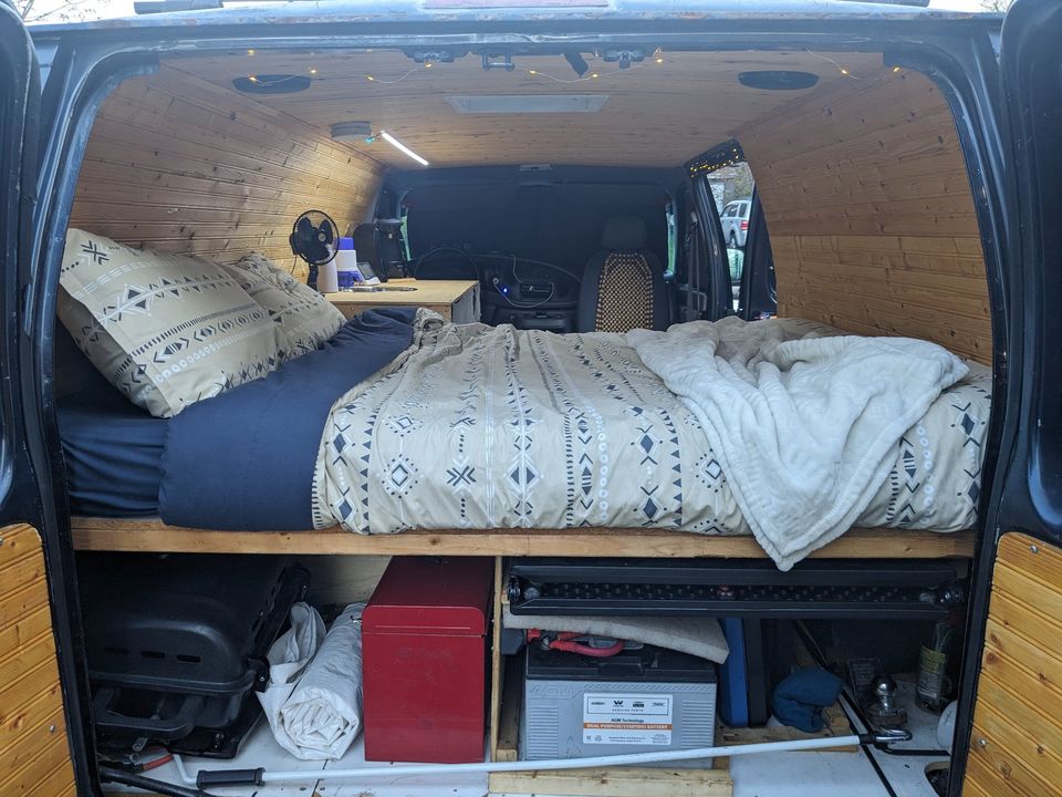 Spacious RV rental van interior with comfy bed, wood-paneled walls, & under-bed storage. Ideal for adventurers.. Ford Econoline 150 1999