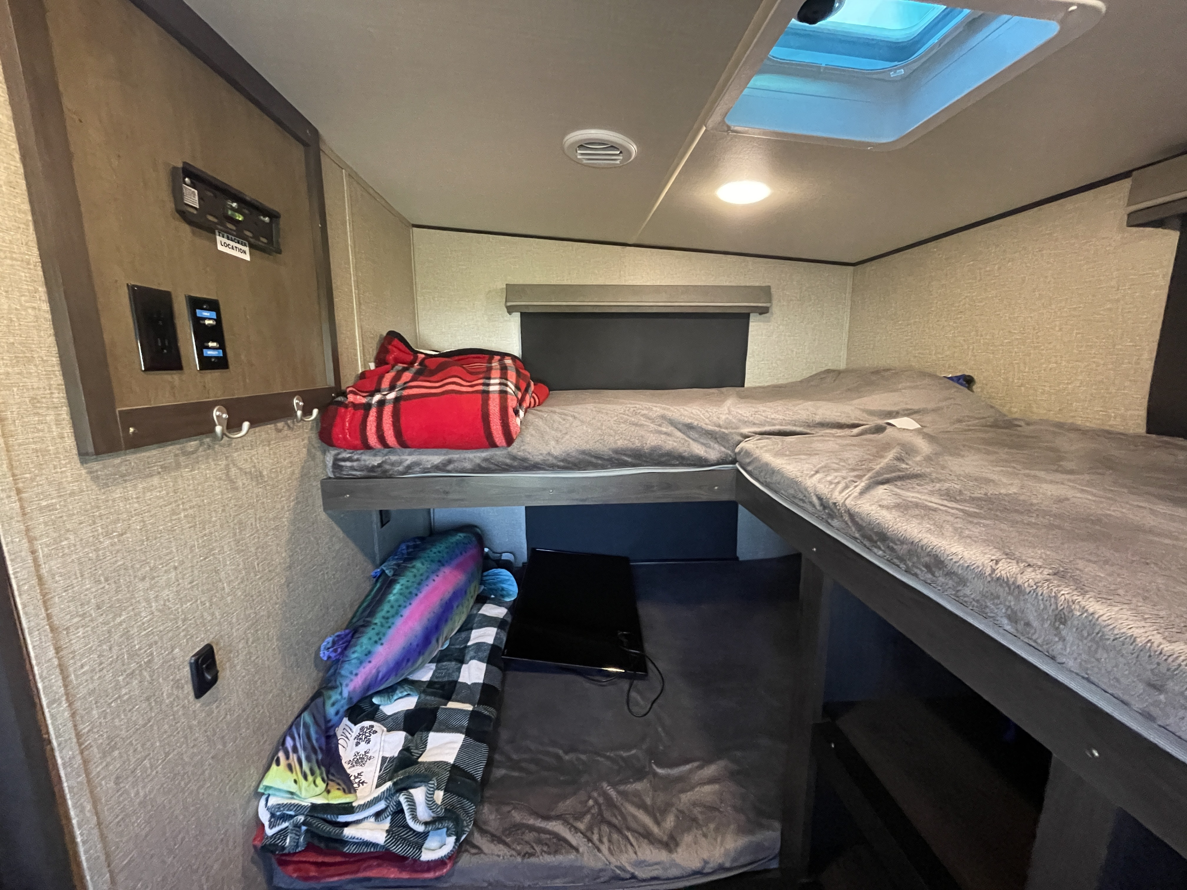 RV rental interior showing comfortable bunk beds, a small TV, blankets, and a ceiling skylight, ideal for rest.. Grand Design Reflection 2021