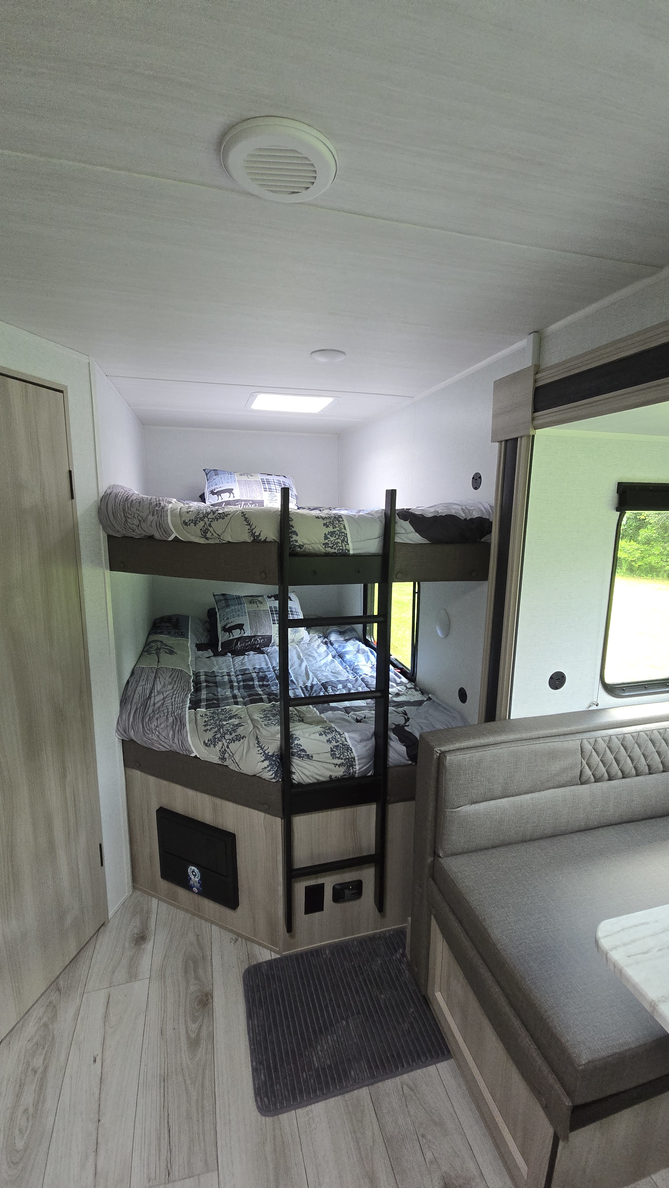 RV rental bunk room: two beds with nature-themed bedding, a ladder, wood-look floors, and adjacent dinette seating.. East to West Silver Lake 2024