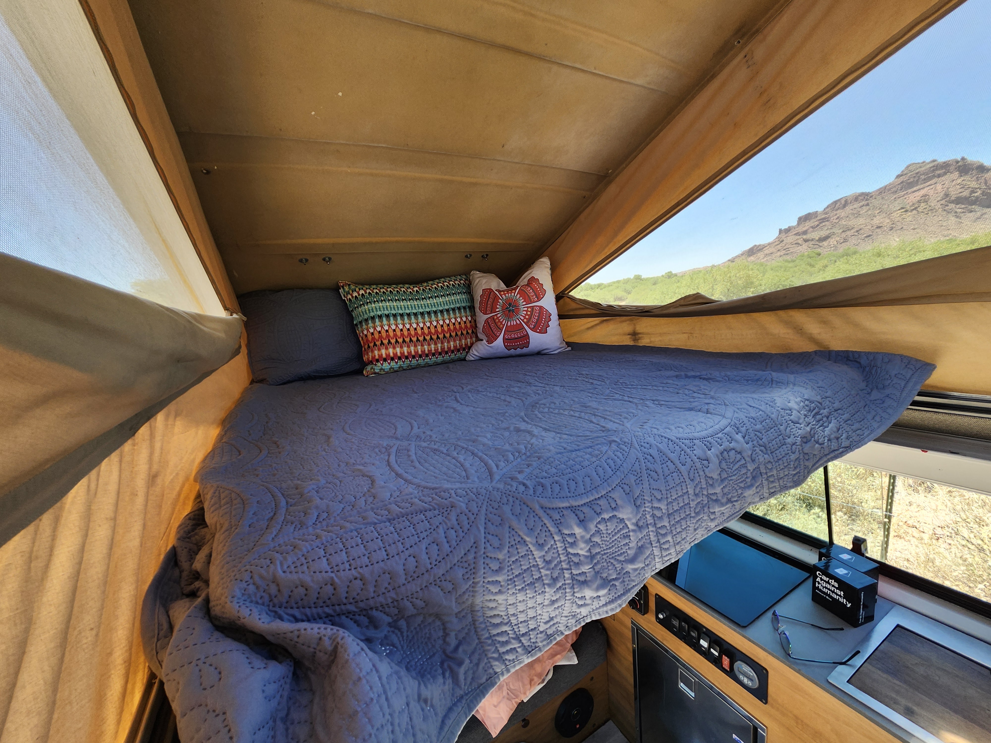 RV rental: Cozy bed with colorful pillows in a pop-top camper, overlooking serene mountains and a well-equipped interior.. Volkswagen Vanagon 1987