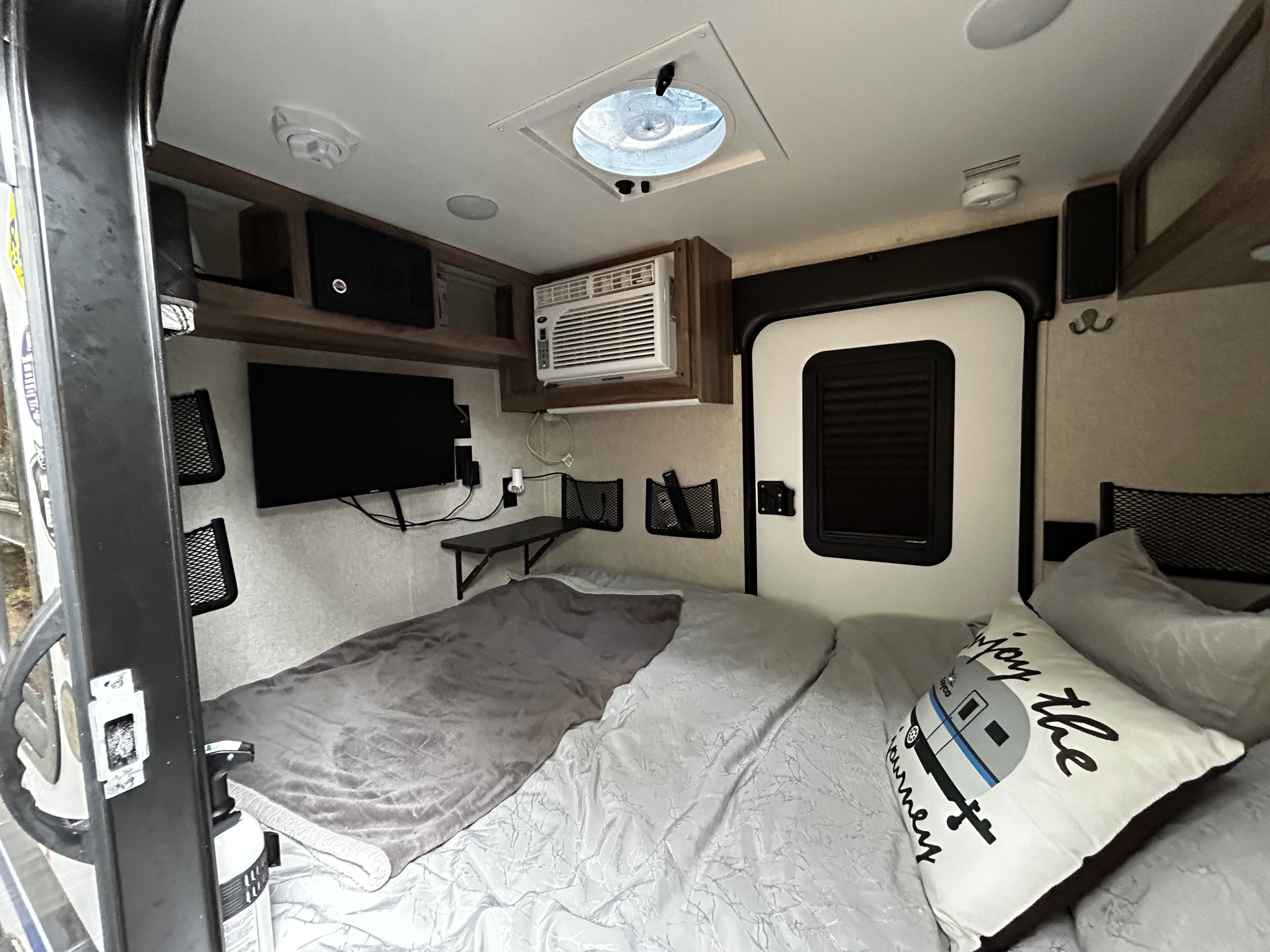 Cozy RV rental bedroom with bed, wall-mounted TV, AC, and storage. Perfect for compact travel.. Jayco Hummingbird 2019