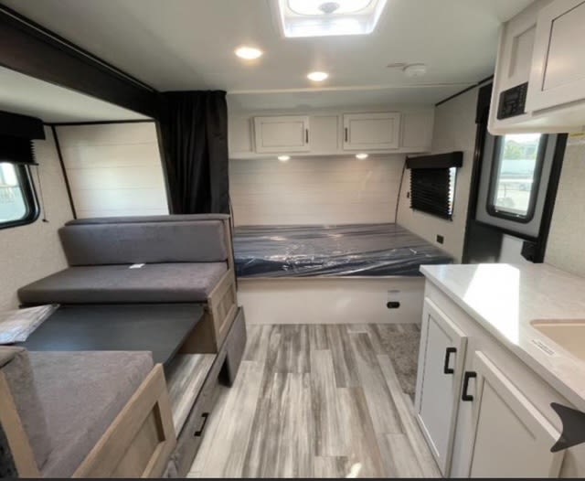 Inside this RV rental: a convertible dinette, main bed, and compact kitchen with white cabinets. Features light wood flooring.. Jayco Jay Flight SLX Baja Edition 2024