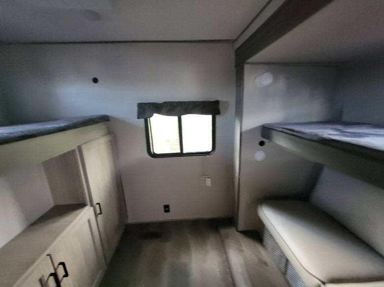 RV rental interior featuring bunk beds on both sides, a central window, and built-in storage cabinets.. Coachmen 323BHDSCK 2024