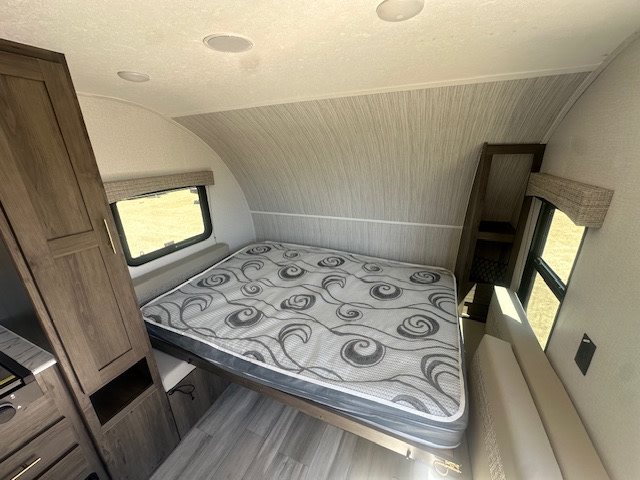 RV rental interior: Comfortable bedroom featuring a patterned bed, wood-grain cabinets, and bright window.. Viking Saga 182DBU 2022