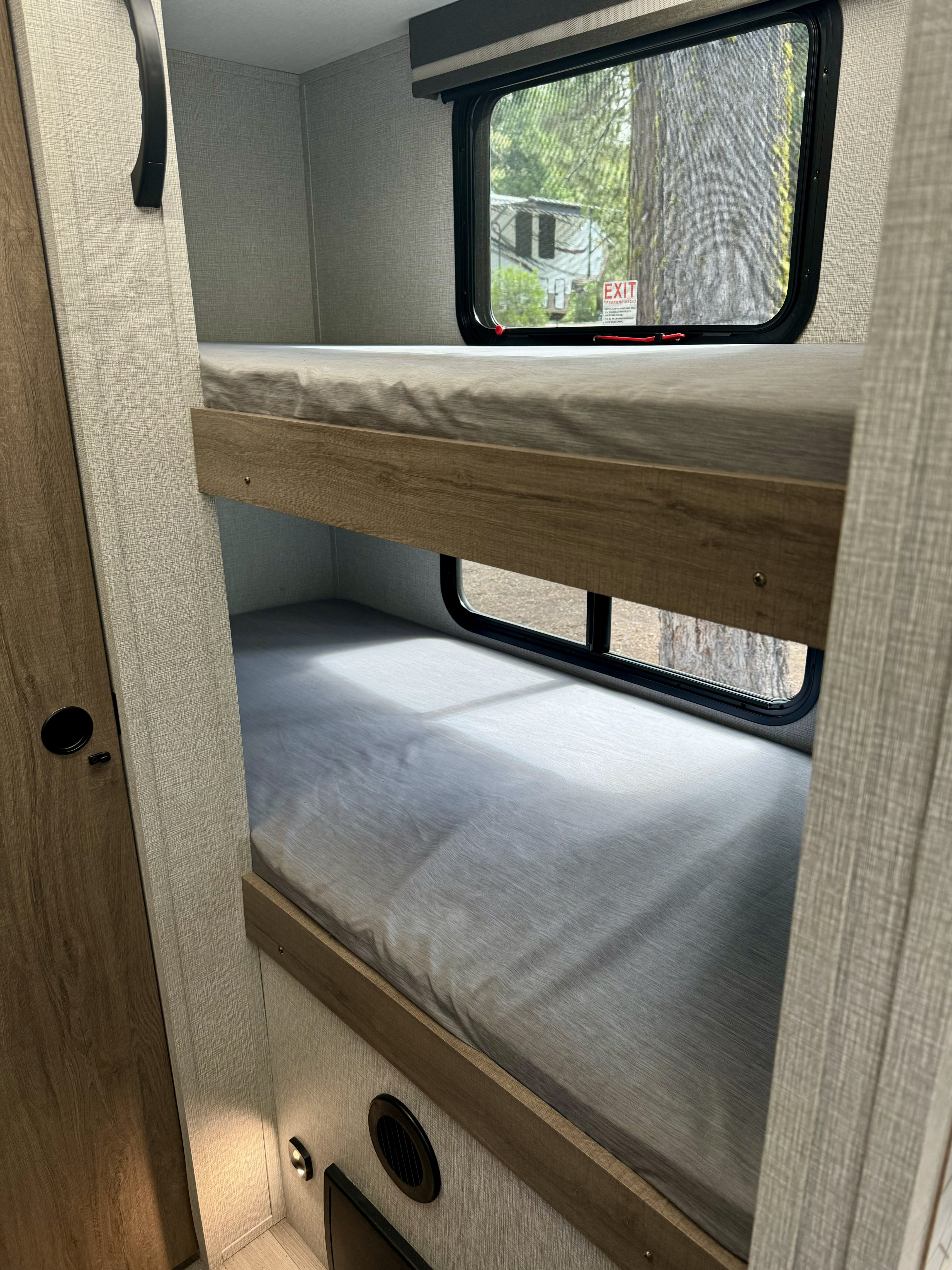 Cozy bunk beds in an RV rental, offering comfortable sleeping quarters with views of nature outside the window.. Grand Design Imagine AIM 2024