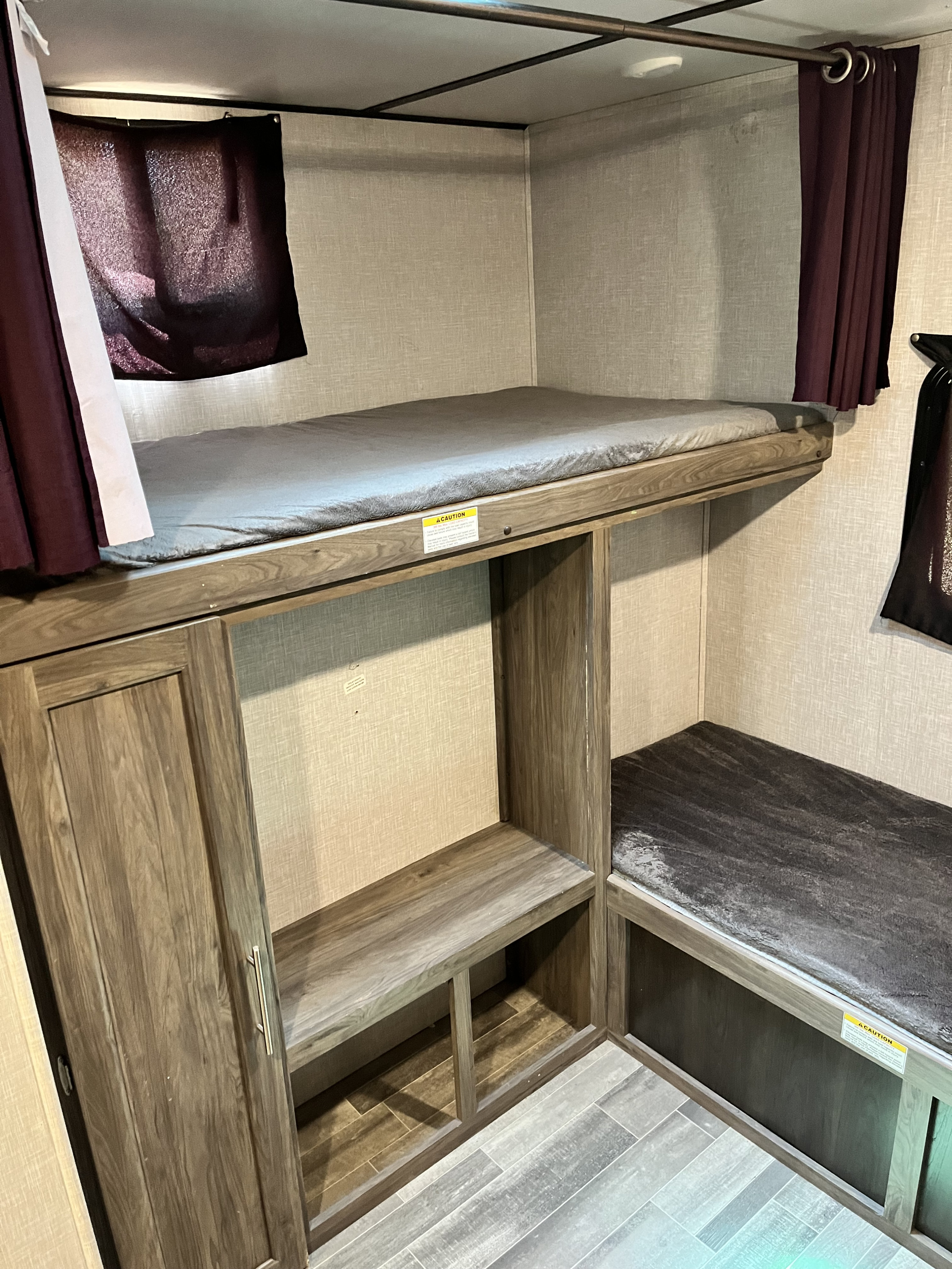 RV rental interior: View of the bunk bed area with an upper mattress, lower seating/bed, and a wood-toned storage unit. Curtains for privacy.. Crossroads RV Zinger 2022