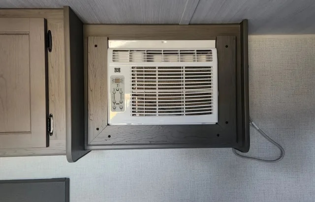 An RV rental's interior shows a white window AC unit installed in a custom wooden frame, ensuring travel comfort.. Keystone RV Hideout Sport 2024
