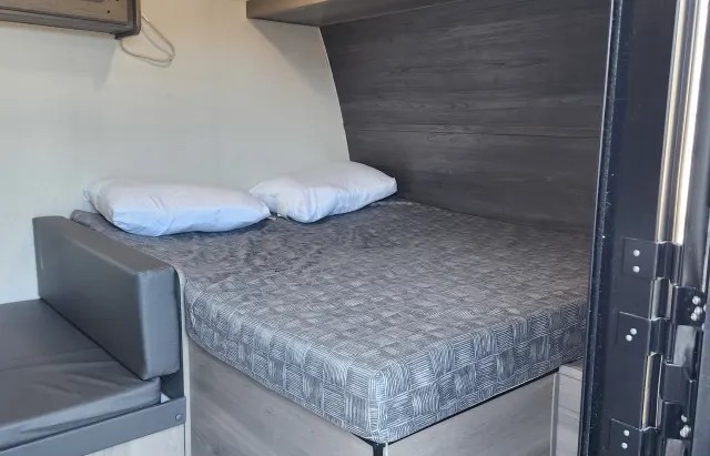 RV rental interior: A compact sleeping area with a gray patterned bed, pillows, and a side bench.. Keystone RV Hideout Sport 2024