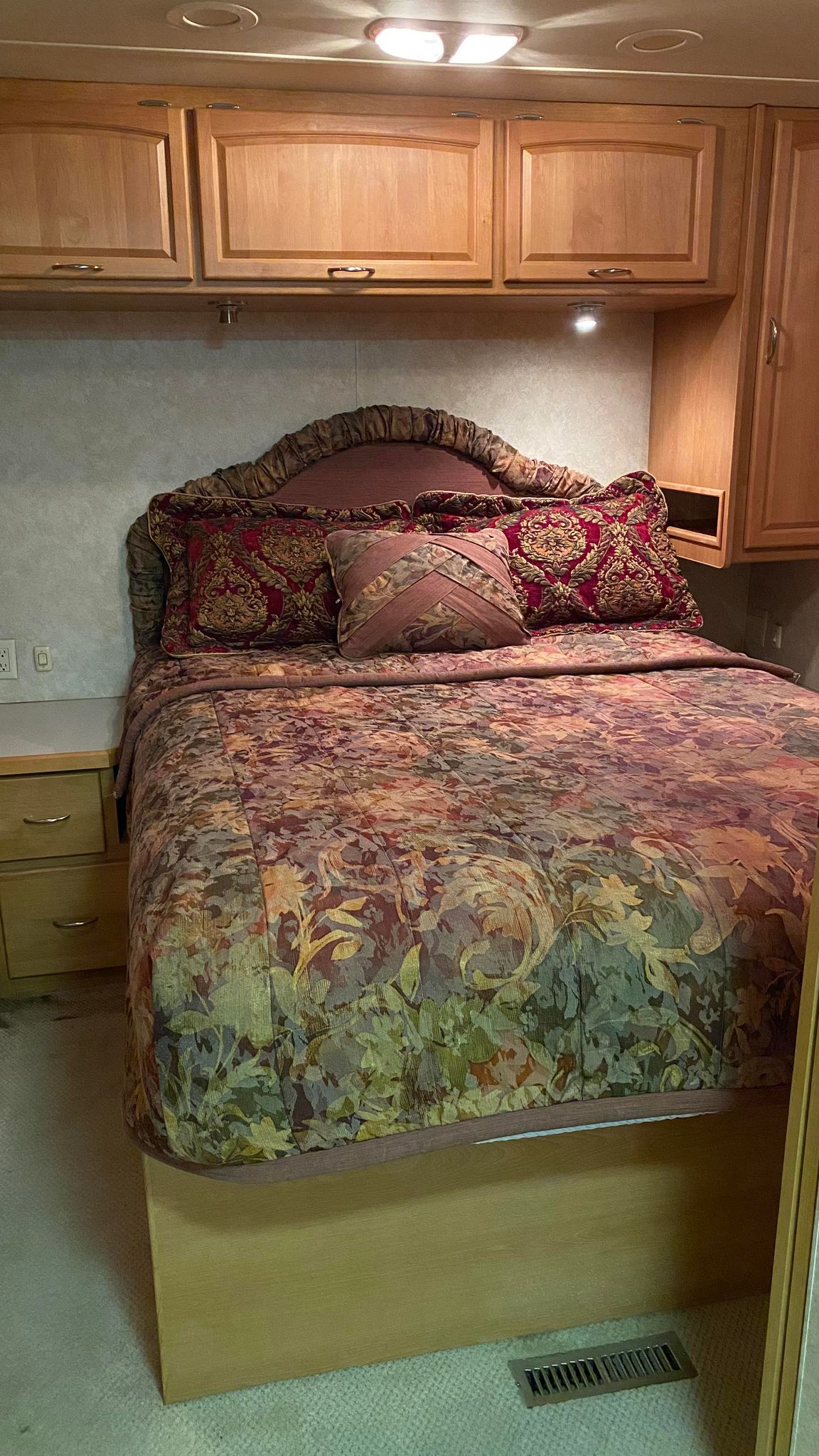 This RV rental's cozy bedroom features a bed with colorful floral bedding, wood cabinets, and overhead lighting.. Holiday Rambler Neptune 2008