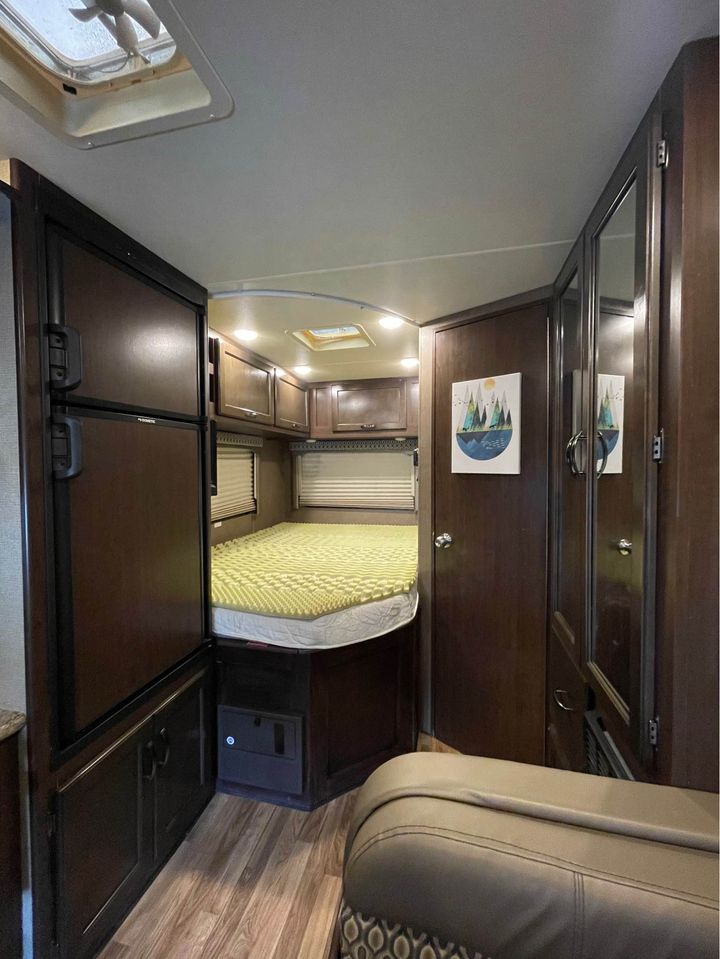 RV rental interior: View of the bedroom area with a light green bed topper, dark wood cabinets, fridge, and wood floors.. Thor Motor Coach Freedom Elite 2019