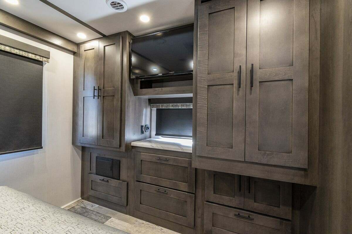 Modern RV rental bedroom featuring dark wood cabinets, a mounted TV, and ample built-in storage.. FR3 FR3 Motorhome 2022