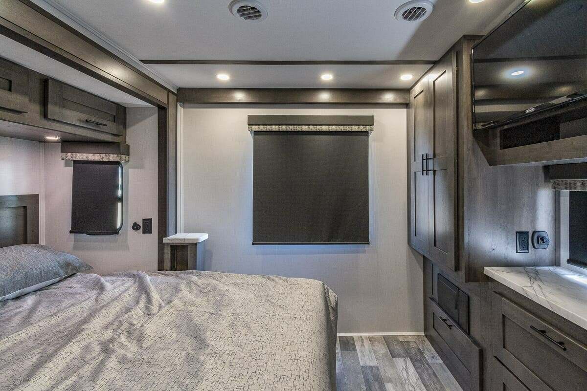 Spacious, modern RV rental bedroom featuring a comfortable bed, overhead storage, and TV. Dark wood accents and blinds.. FR3 FR3 Motorhome 2022