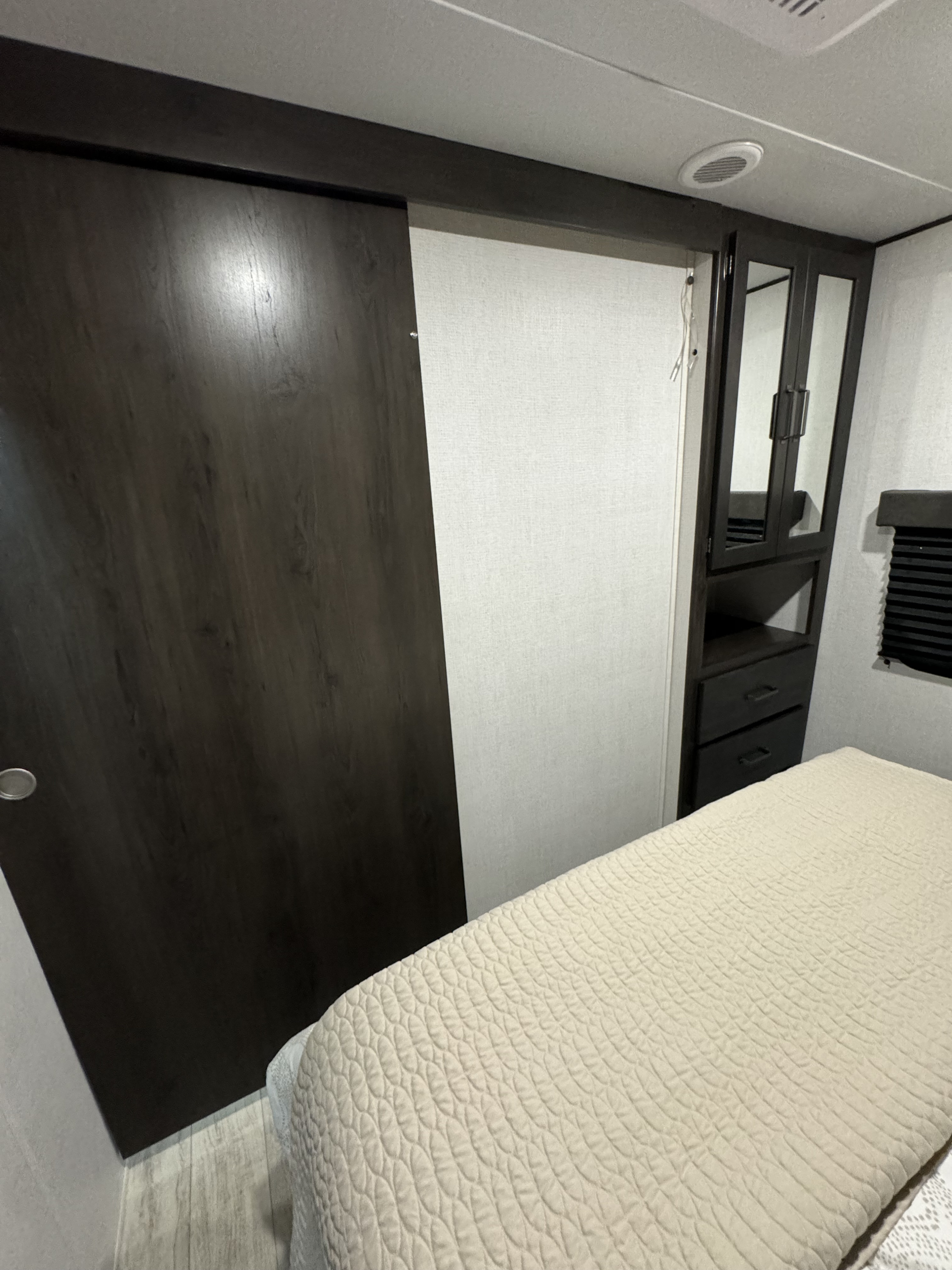 RV rental bedroom: dark sliding door, mirrored closet, drawers, and light quilted bed for compact comfort.. Grand Design 27MAV 2024