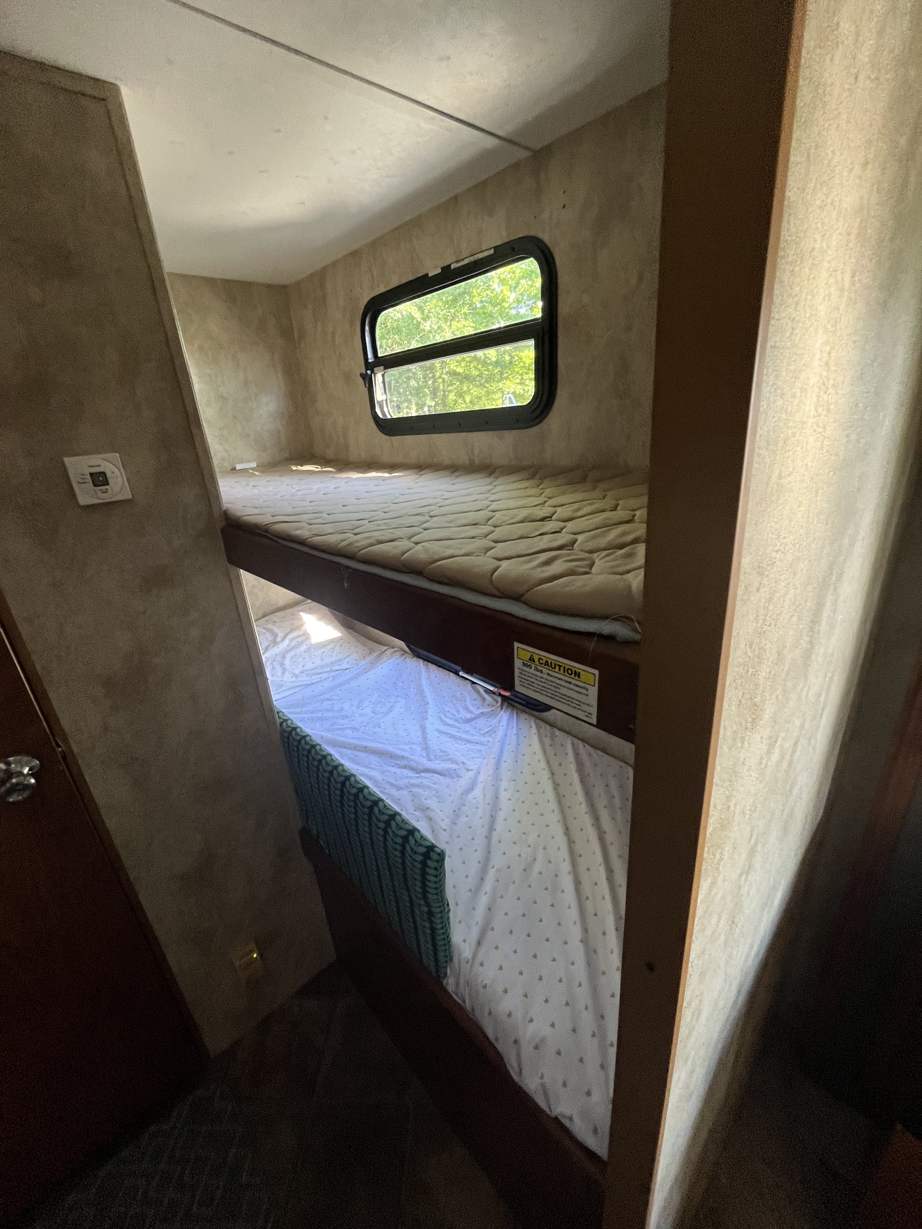 Inside an RV rental: Compact sleeping area with upper and lower bunk beds, window, and wall controls.. Keystone RV Passport Ultra 2013