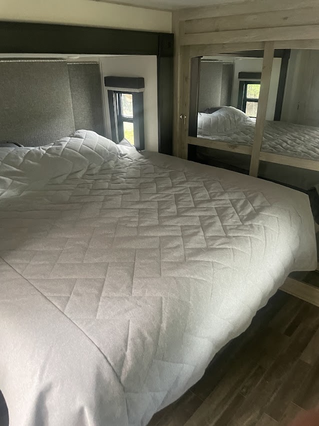 Cozy RV rental bedroom with a comfortable quilted bed, bedside windows, and mirrored closet for your travels.. Keystone RV Avalanche 2021