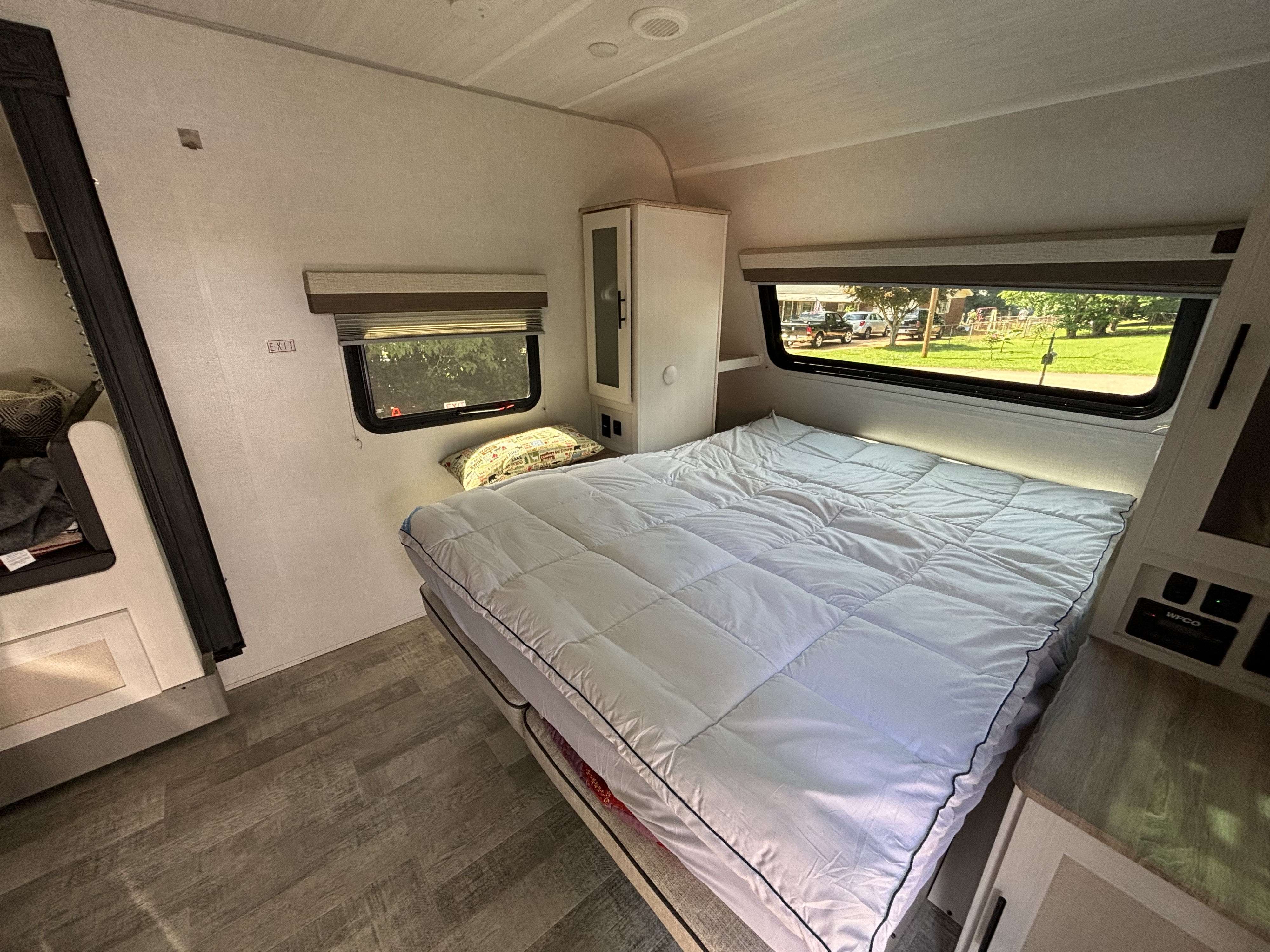 Cozy RV rental bedroom with white bedding, window view, and built-in storage.. No Boundaries 20 2023