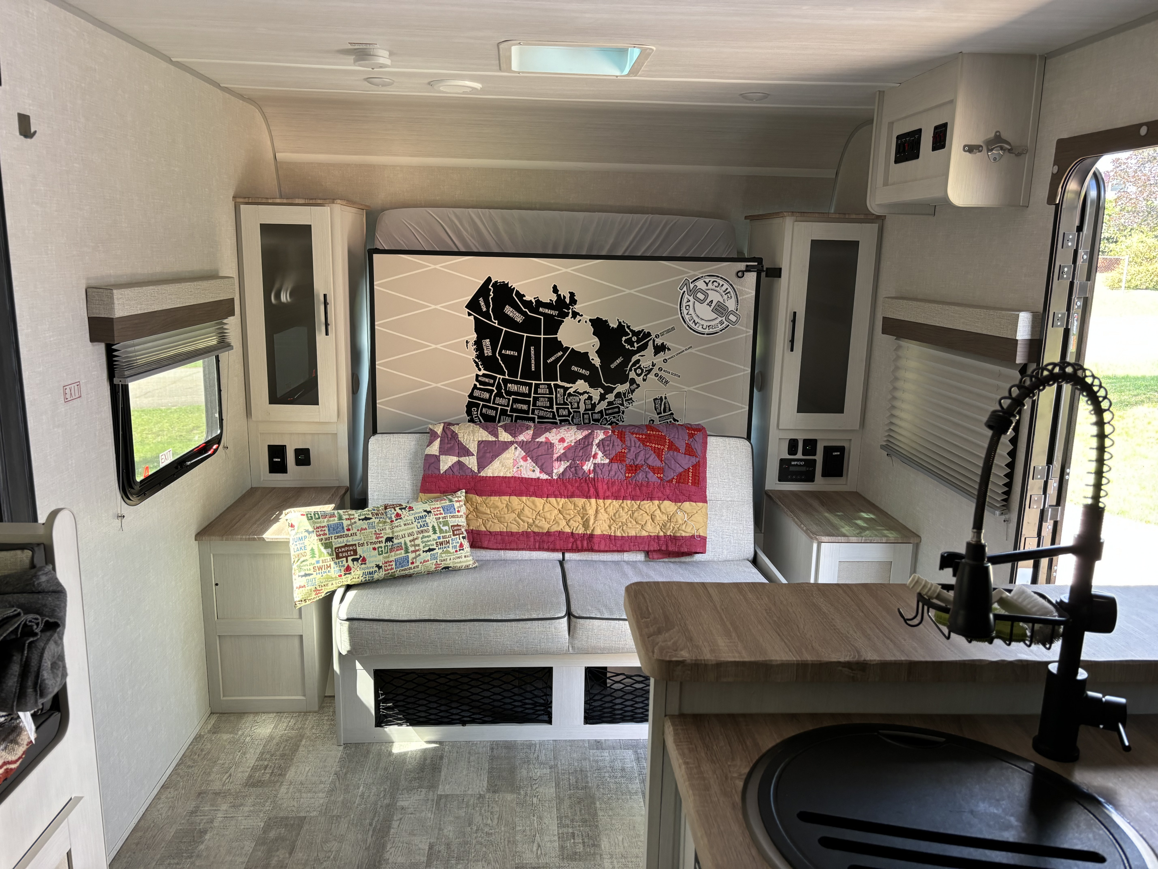 This RV rental interior features a cozy sofa bed, map mural, and functional kitchen, ready for your next adventure.. No Boundaries 20 2023