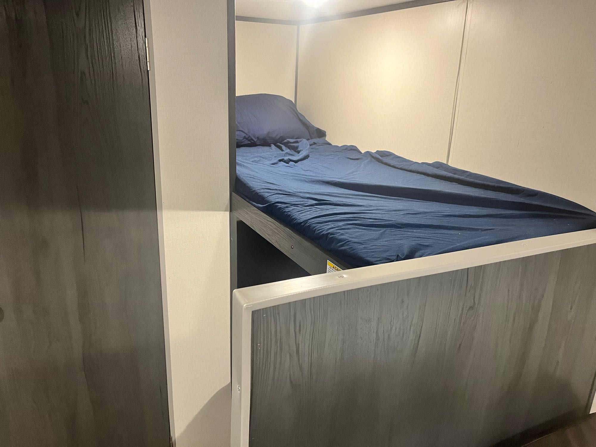 Compact bunk bed with dark blue bedding inside an RV rental, offering a cozy sleeping area.. Aspen Trail LE 2021