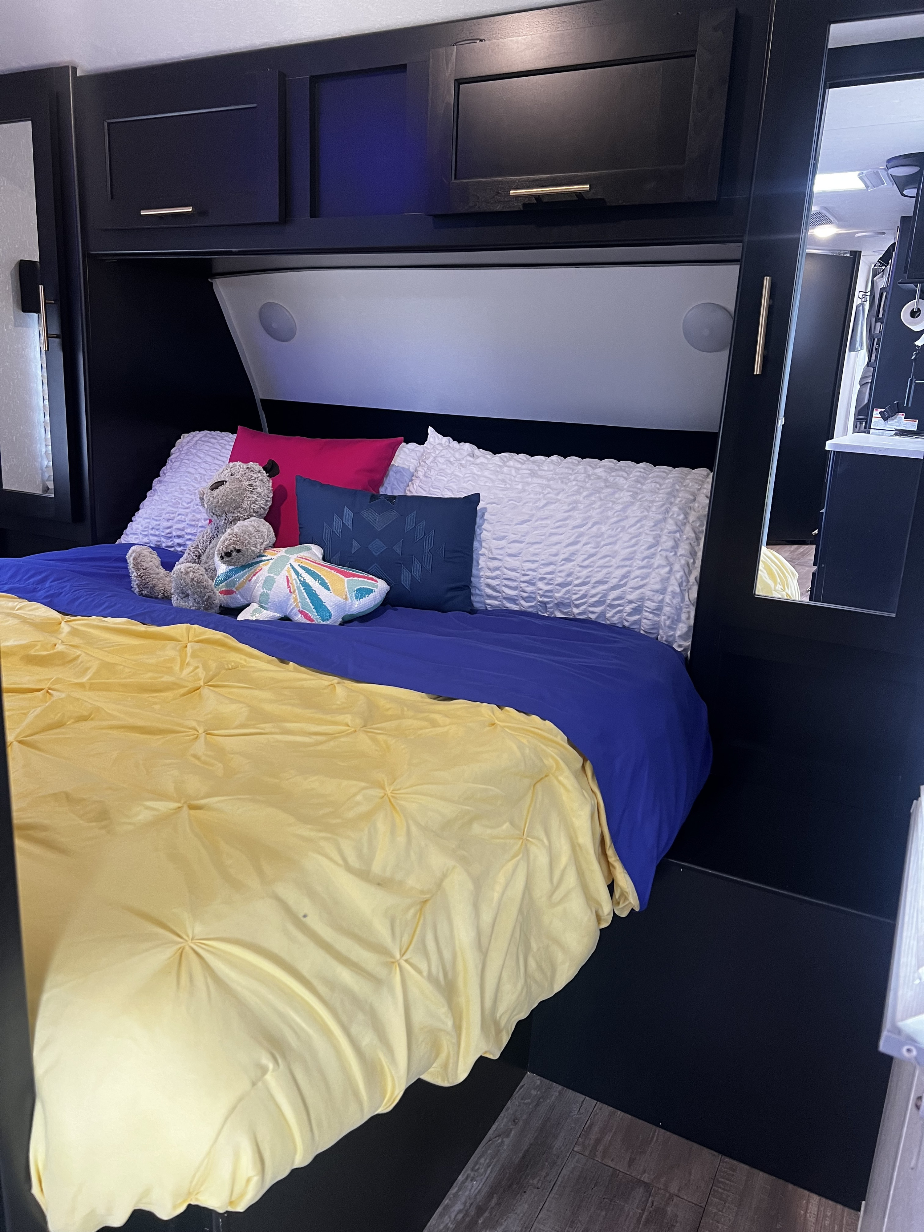 Cozy RV rental bedroom featuring dark cabinetry, a blue and yellow bed, pillows, and a teddy bear.. Forest River Cherokee Grey Wolf 2021