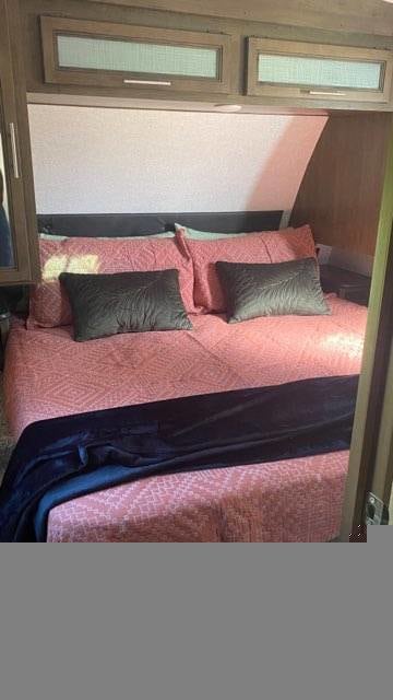 RV rental bedroom: cozy bed with pink comforter, dark pillows, and overhead storage, perfect for your next trip.. Keystone RV Cougar 2020