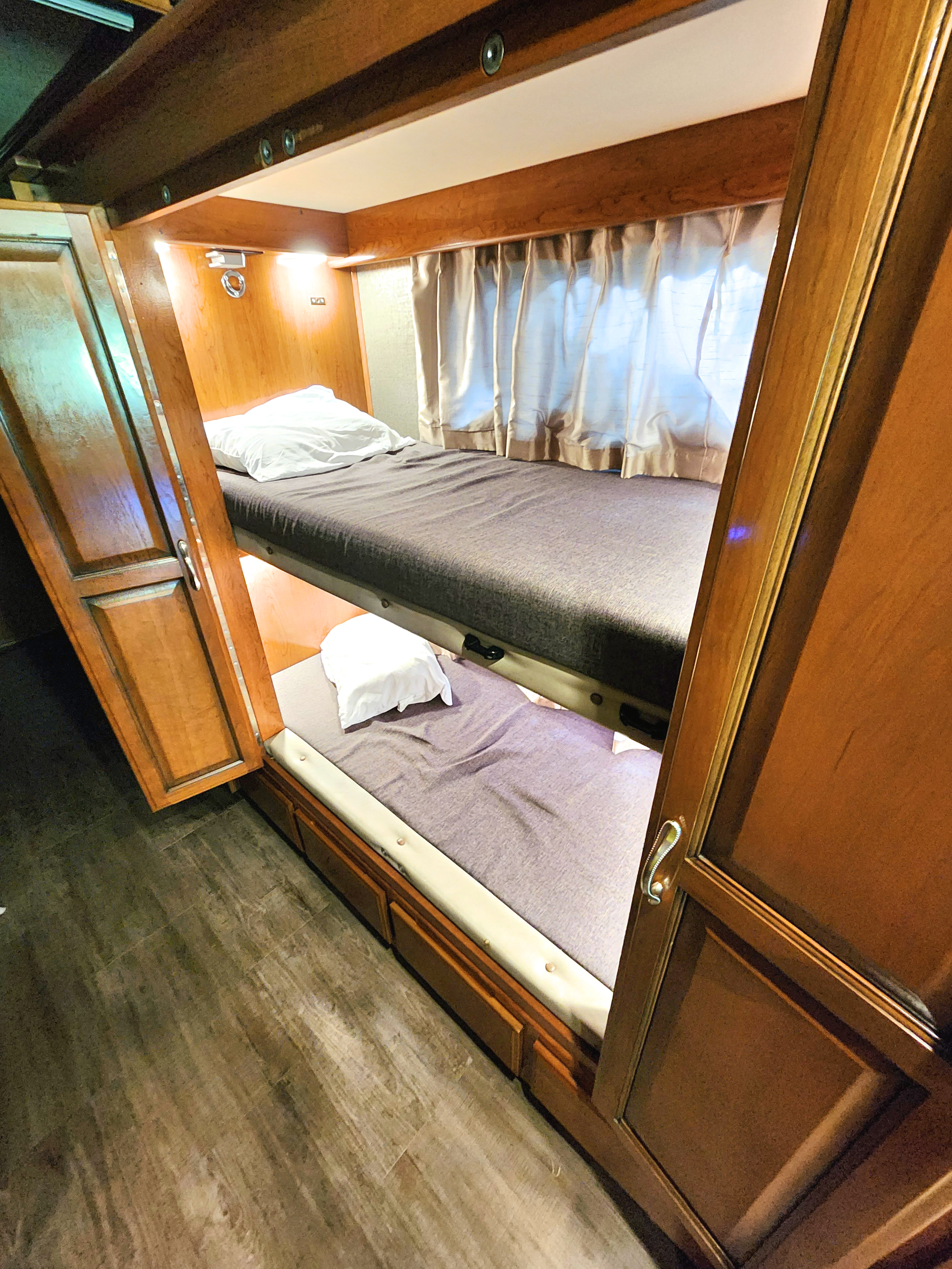 Explore this RV rental's functional interior featuring stacked bunk beds with comfy grey mattresses and wooden cabinets.. Fleetwood Bounder 2018