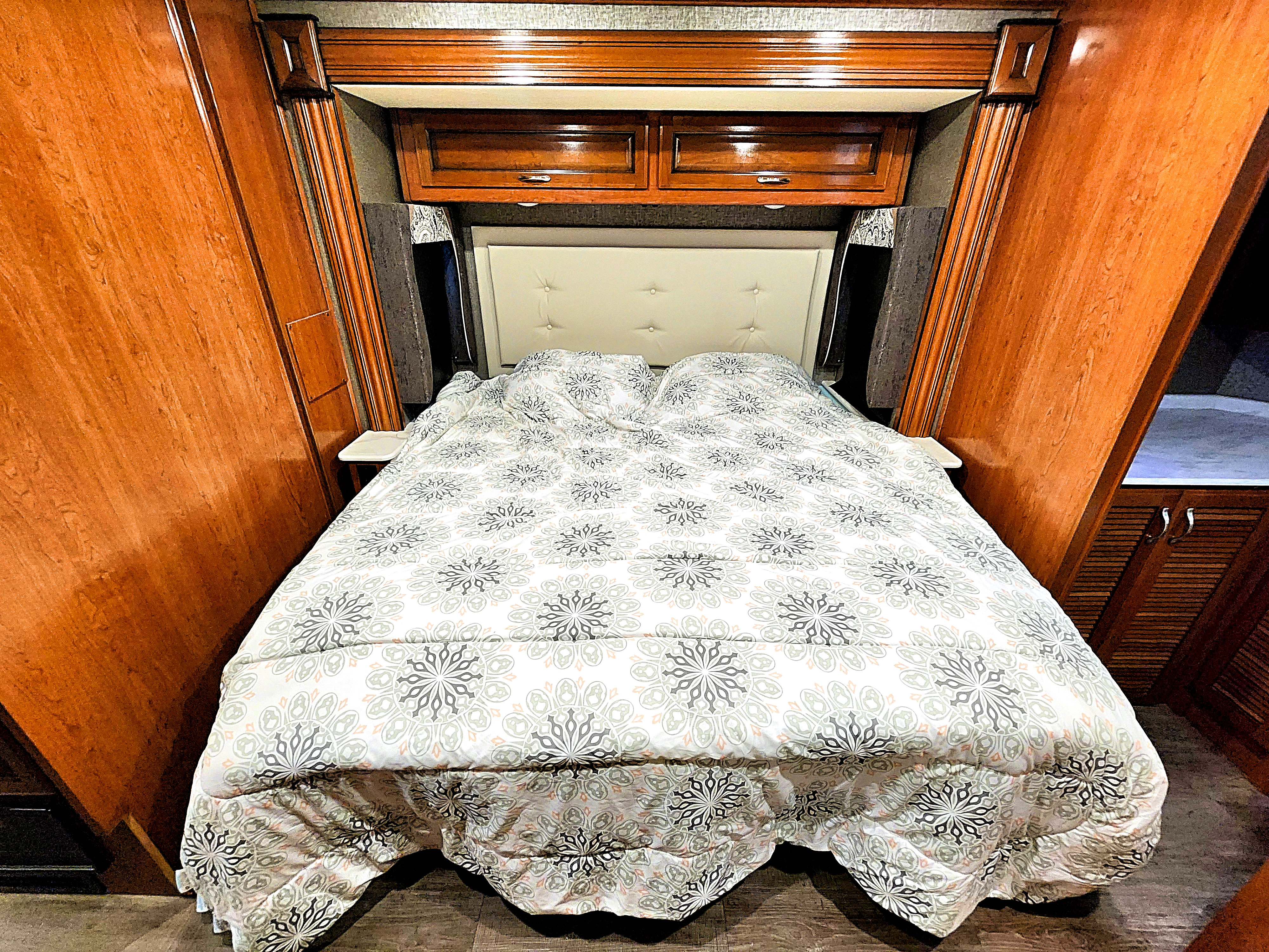 Inside this RV rental bedroom: a comfortable bed with a patterned comforter, upholstered headboard, and wooden storage.. Fleetwood Bounder 2018