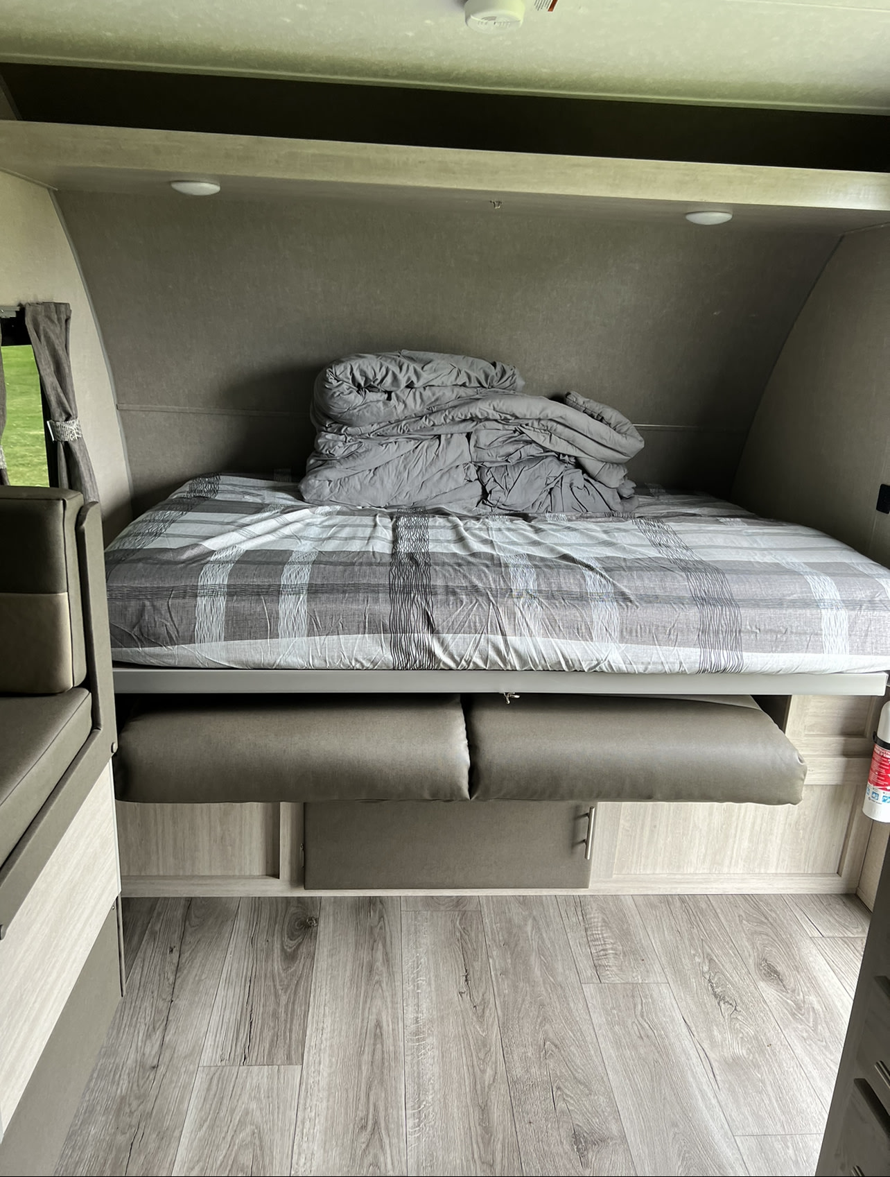 Compact RV rental interior featuring a convertible bed with plaid bedding, storage, and wood-look flooring.. Forest River Aurora Aurora 2022