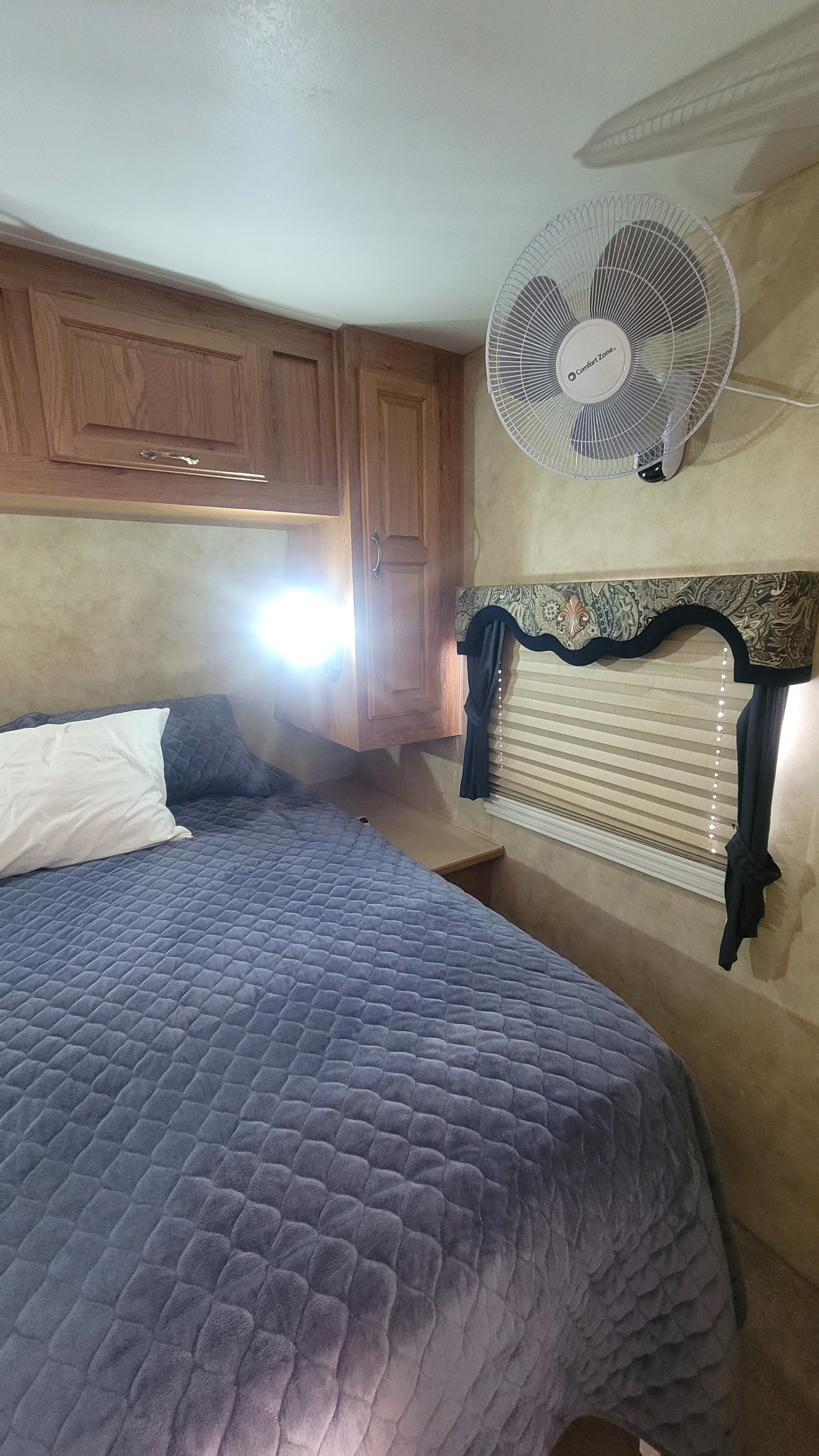 RV rental bedroom: A comfortable bed, wood cabinets, and a wall fan. Bright light on the left.. Jayco Eagle 2006