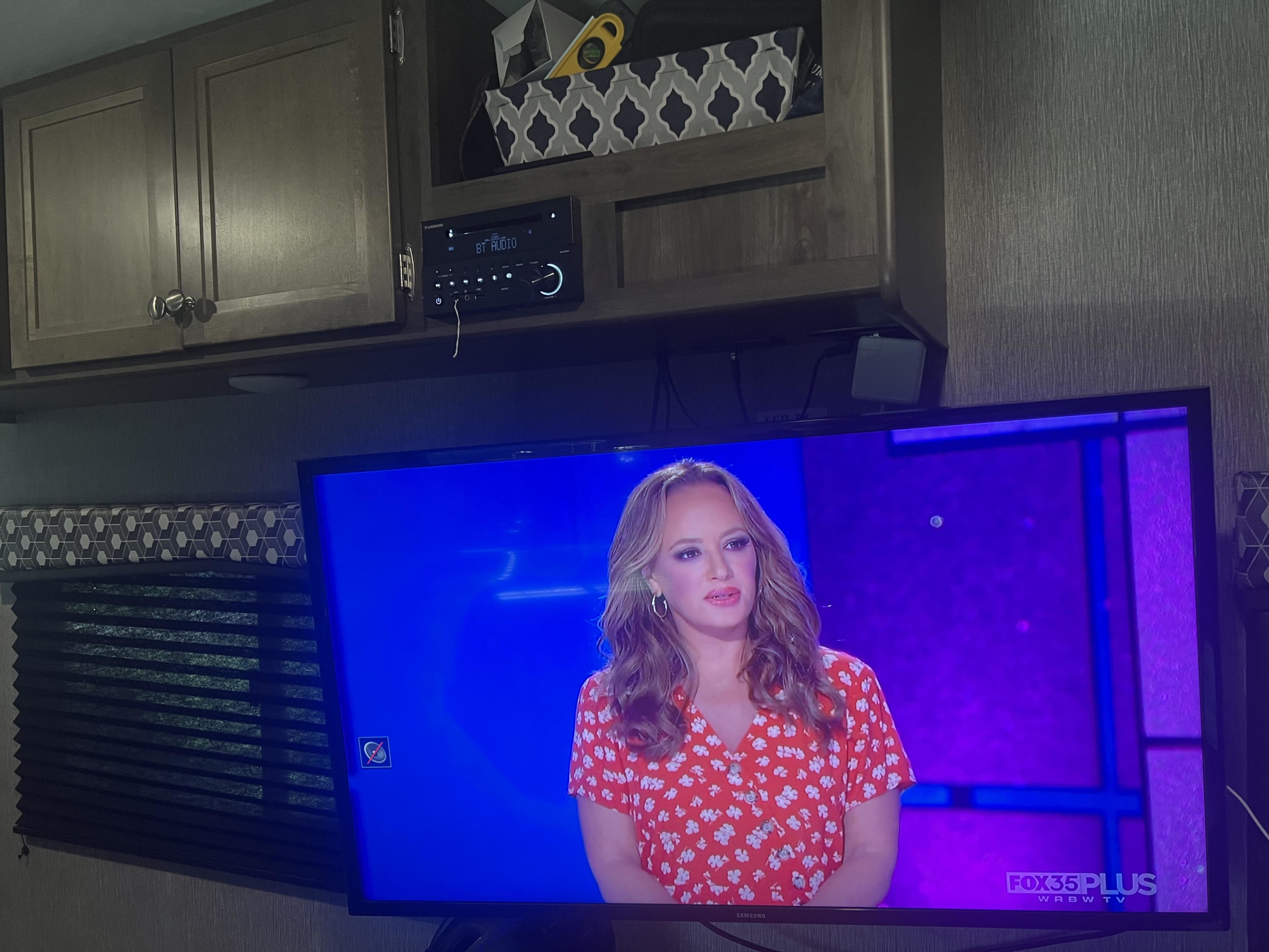 RV rental interior: A TV displaying a woman, a Furrion audio system, and wood cabinets. Enjoy entertainment in this cozy camper.. Coleman Lantern Toy Hauler Series M-250TQ- Pet Friendly + 6 person tent 2020