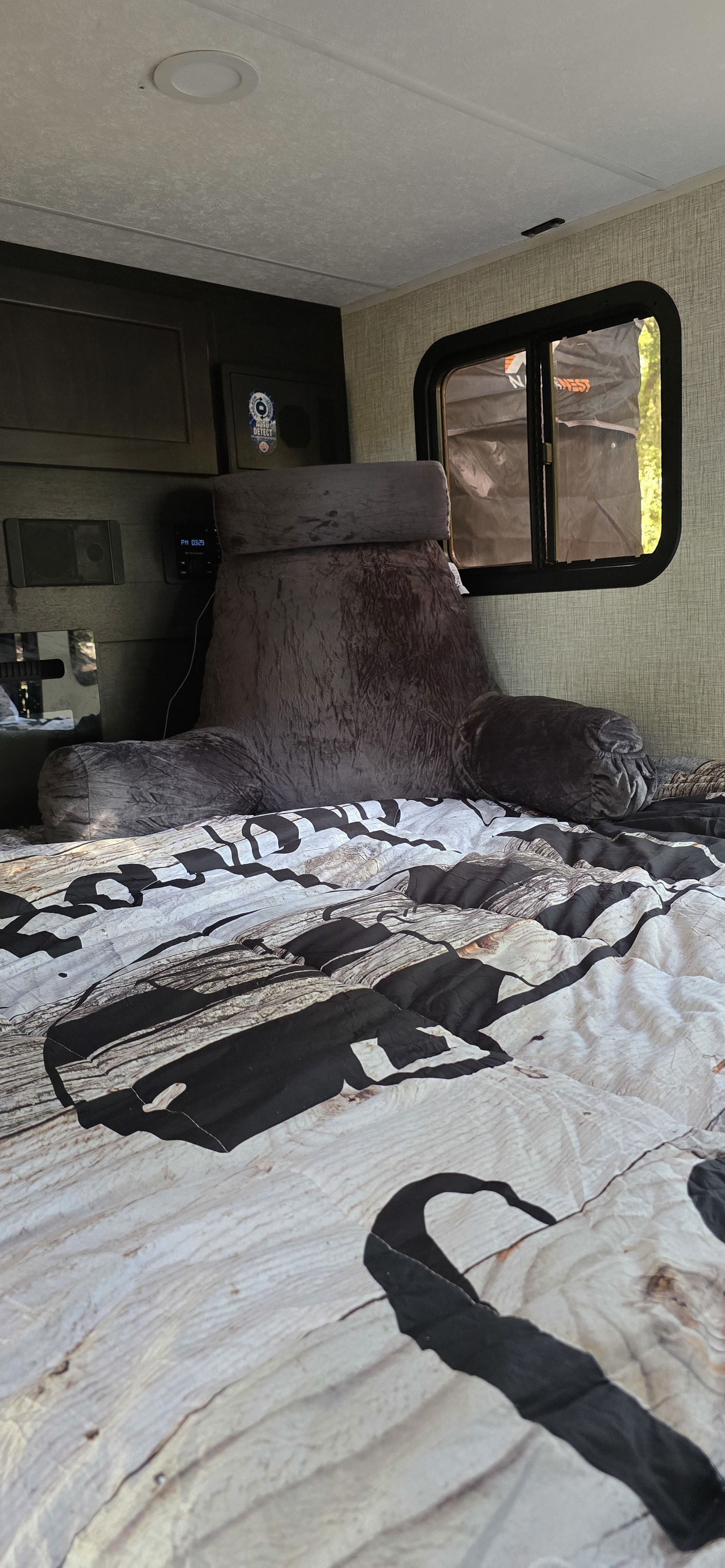 Cozy RV rental bedroom with wood-grain bedding, a backrest pillow, and a window view. Perfect for travel comfort.. Braxton Creek Bushwhacker 2024