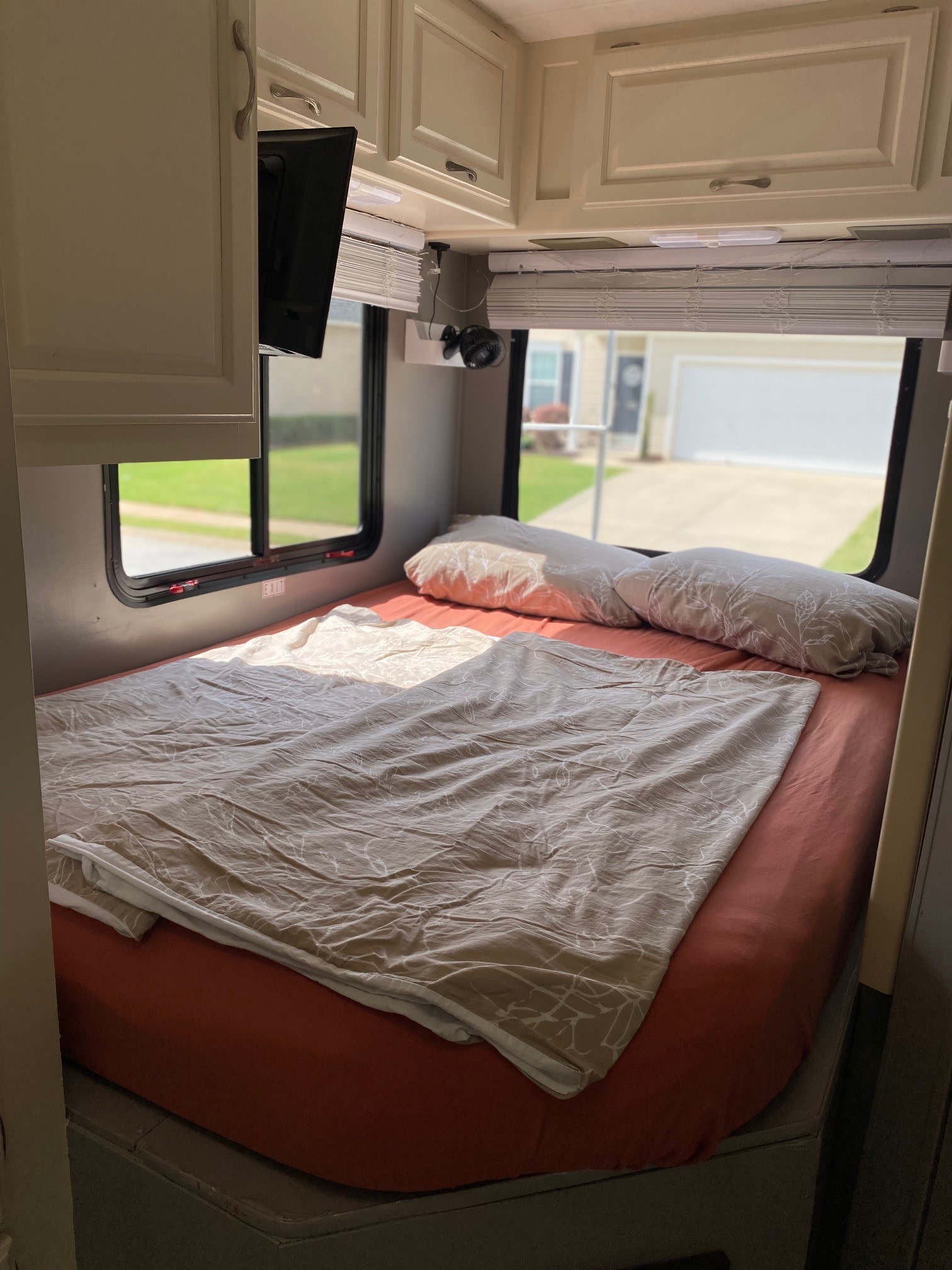 Inside an RV rental, a sunlit bedroom features a bed with orange sheets, pillows, and overhead cabinets.. Four Winds 5000 2008