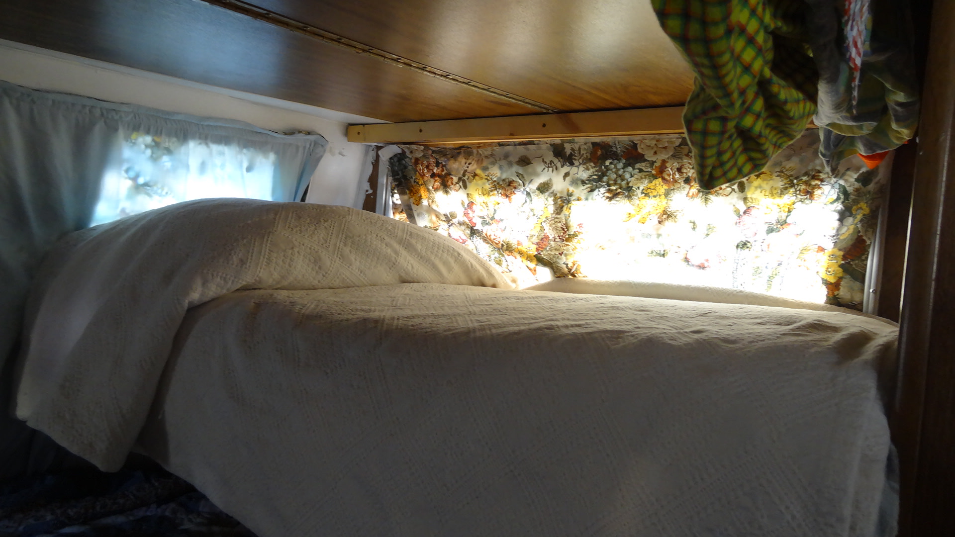 Cozy RV rental bed with white bedding, floral curtains, & bright window light. Perfect for travel comfort.. Vintage Trailers Skylark 180 1979